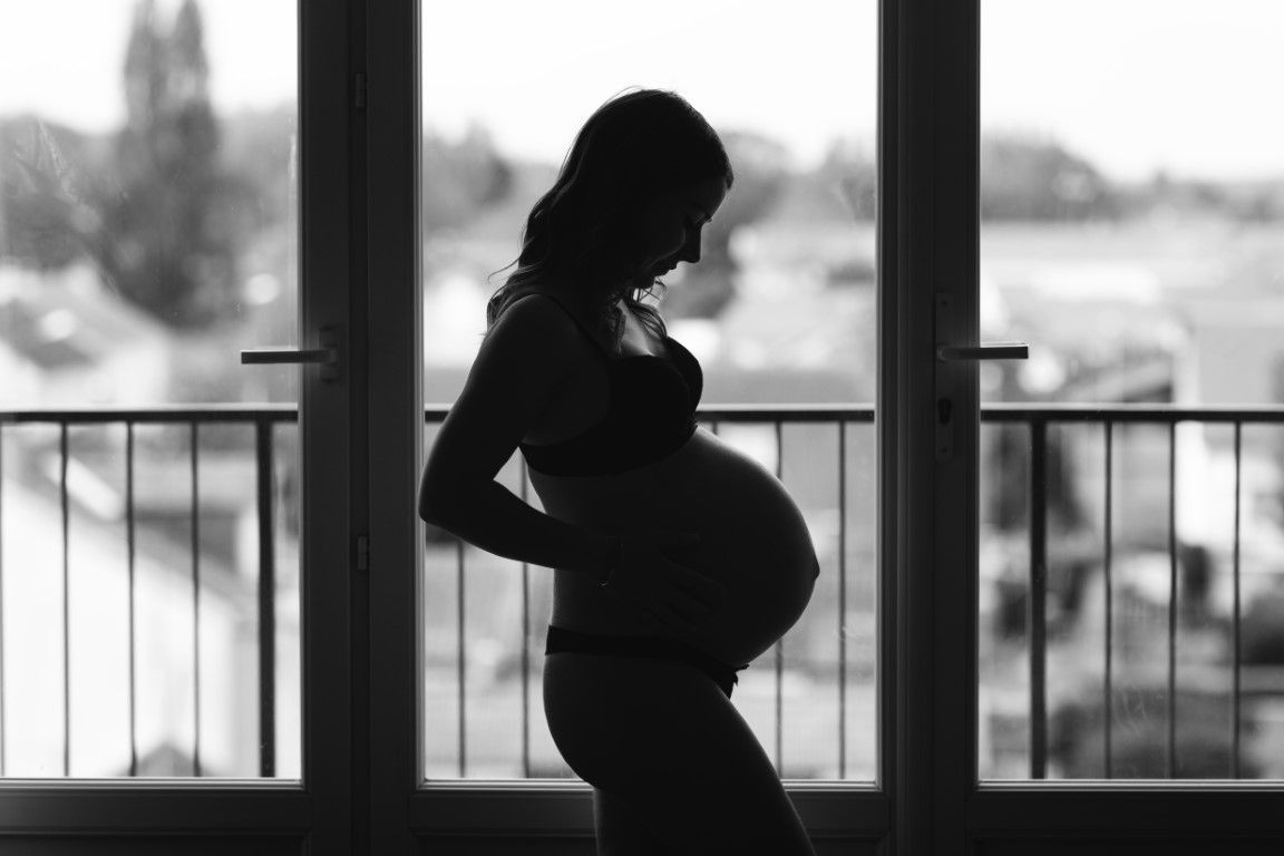 Silhouette en noir et blanc d'une femme enceinte debout près d'une fenêtre, tenant son ventre.