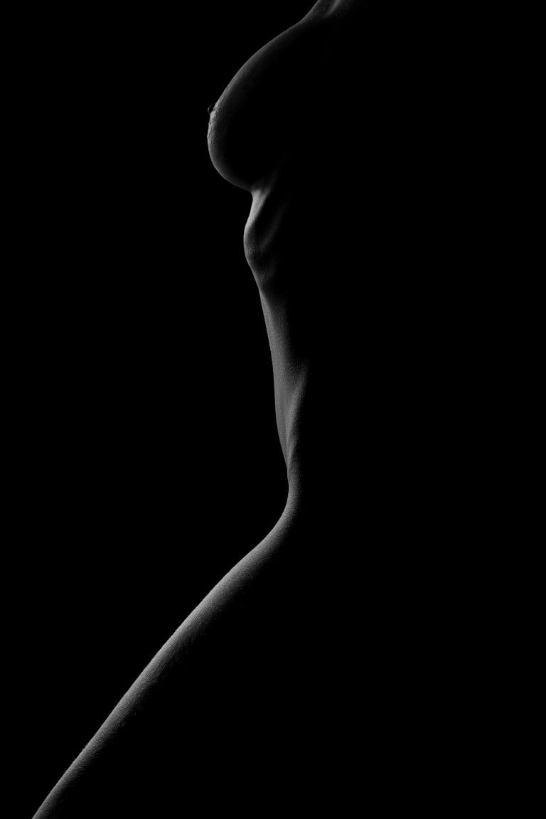 Black and white artistic silhouette photograph highlighting the elegant curves of a human form against a dark background.