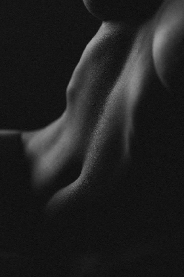 Photo artistique en noir et blanc d'un nu féminin capturant les courbes élégantes d'un torse féminin dans une ombre mystérieuse.