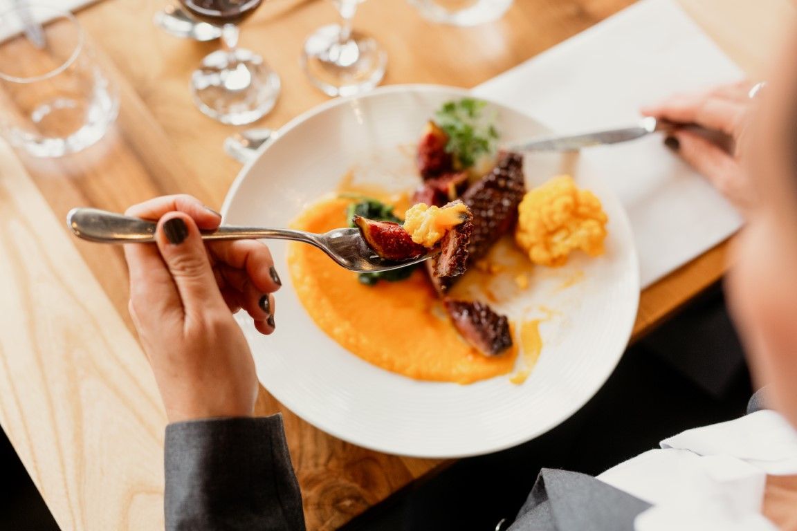 Person eating a gourmet meat dish with orange puree on a white plate at a restaurant.