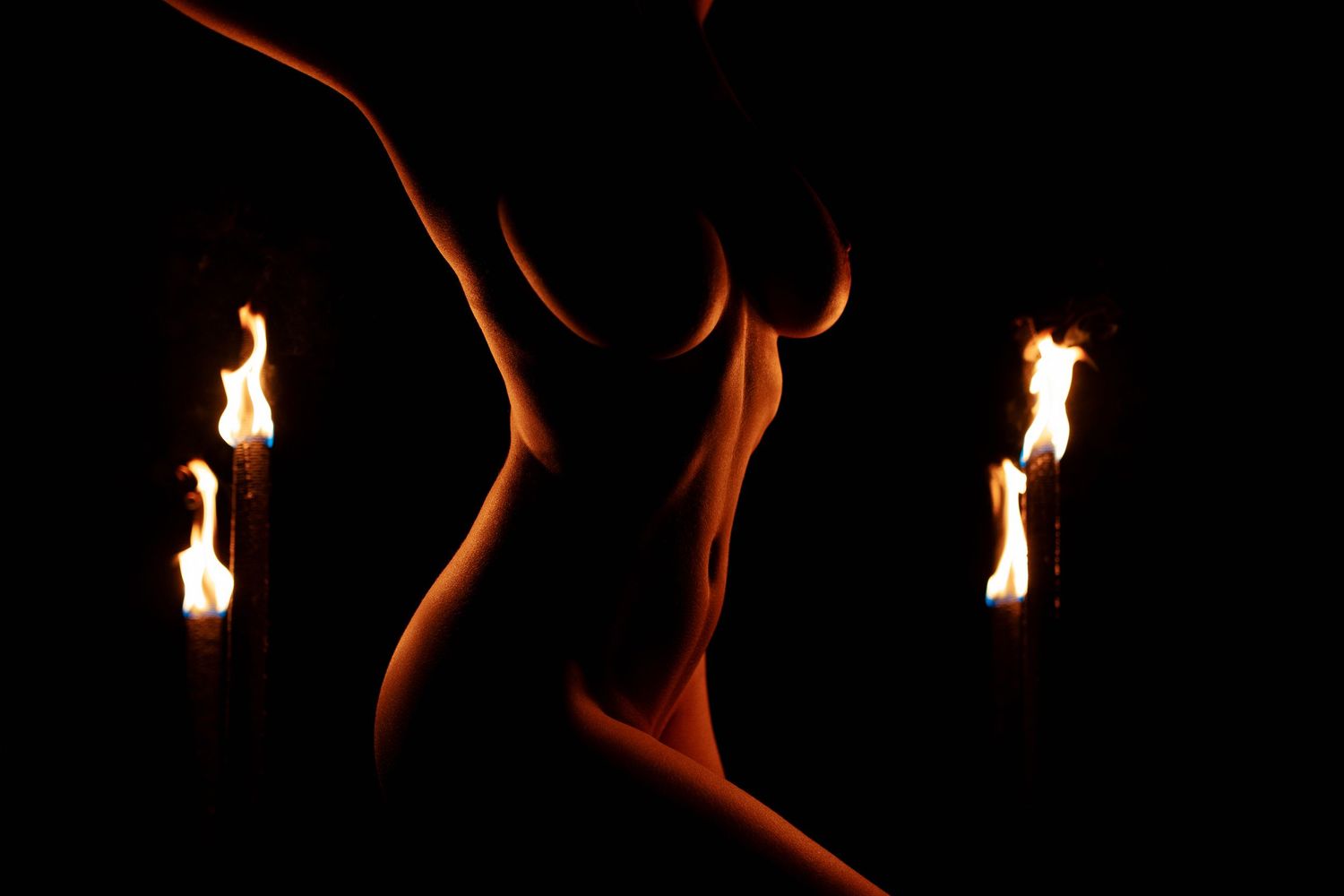 Silhouette of a nude female figure illuminated by three flames against a dark background.