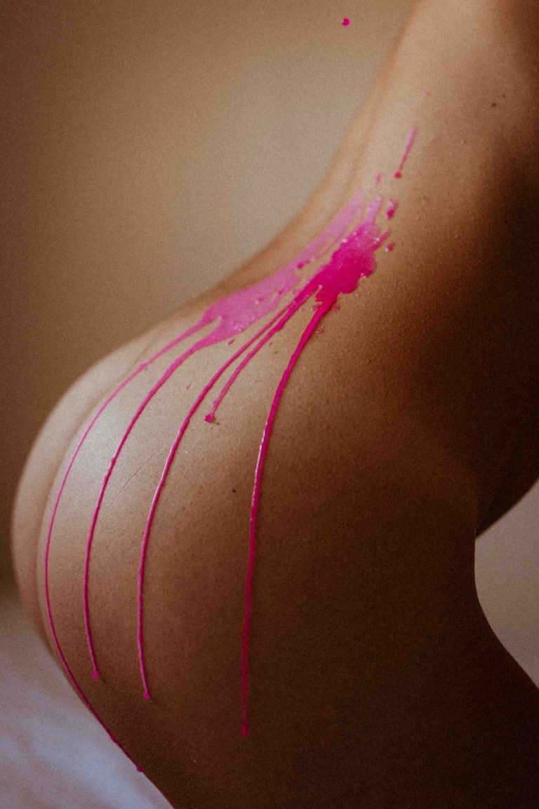 Artistic body photography featuring vibrant pink paint dripping down bare skin in elegant streaks.