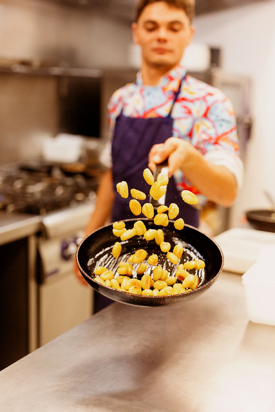 Chef tossing golden gnocchi in a black skillet in a professional kitchen.