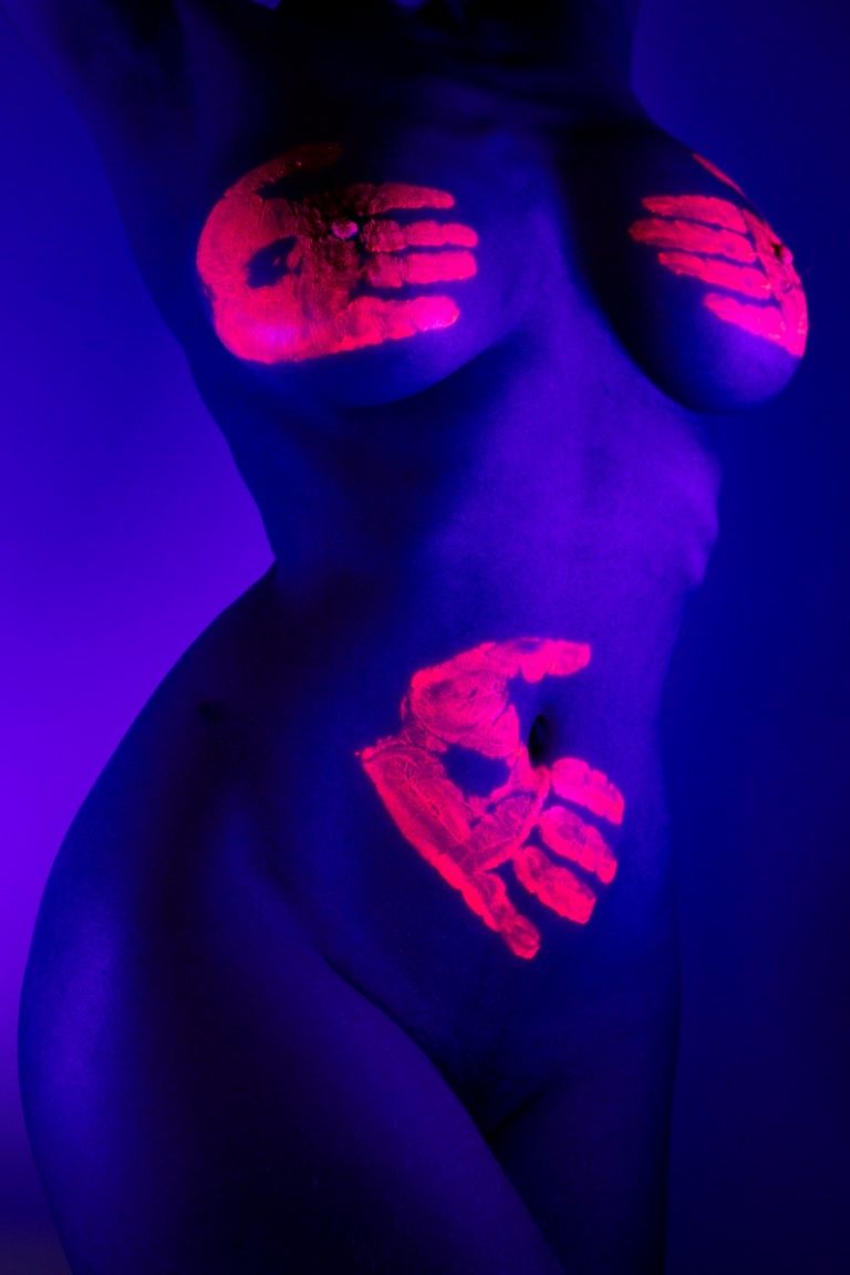Peinture corporelle artistique de nu avec des empreintes de mains fluorescentes rouges UV sur le torse féminin sous lumière noire.