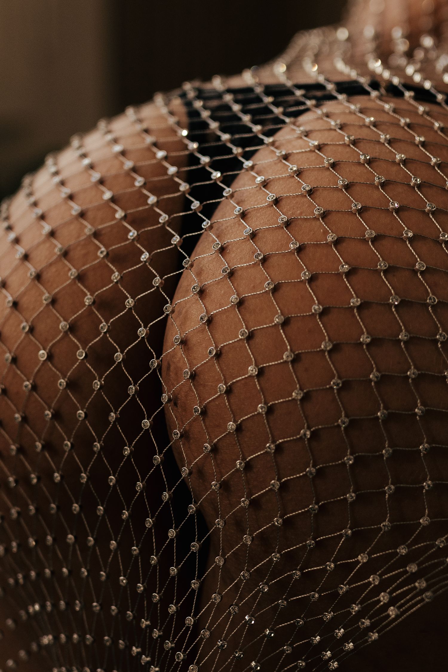 Close-up of sparkling rhinestone fishnet fabric draped over skin, showcasing intricate diamond-shaped mesh pattern.