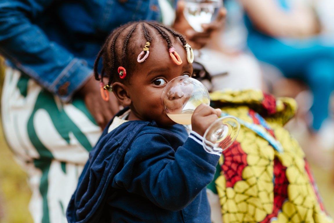 Une jeune fille africaine, les cheveux tressés et ornés de barrettes, souffle des bulles lors d'un événement en plein air.