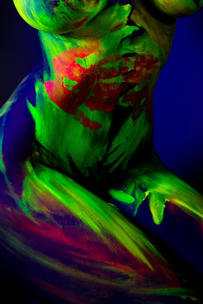 Close-up of a human torso covered in vibrant neon UV body paint glowing green and red under black light.