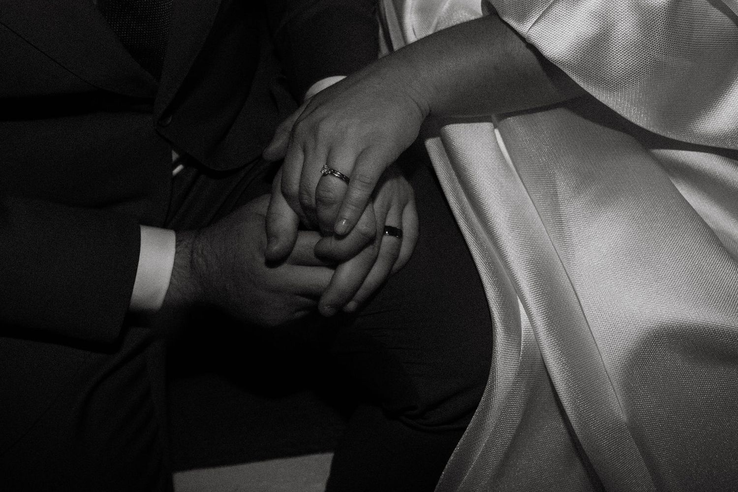Black and white close-up of a bride and groom holding hands, showcasing a diamond engagement ring.