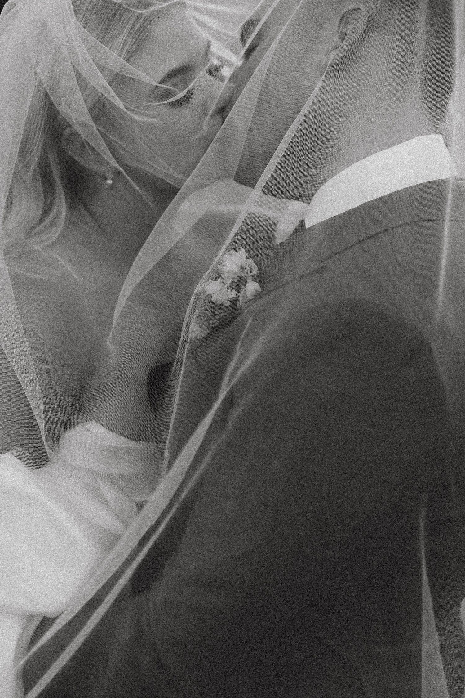 Black and white close-up of bride and groom embracing under a flowing wedding veil.