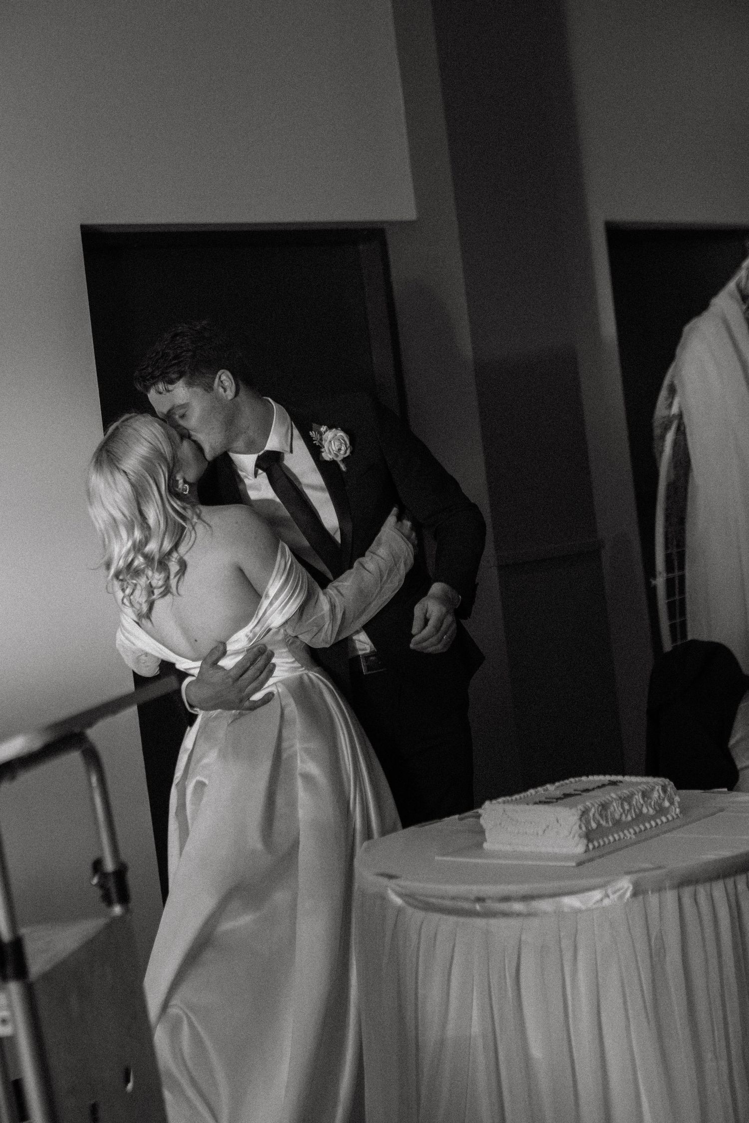 Bride and groom sharing romantic kiss near wedding cake, elegant black and white reception photo.