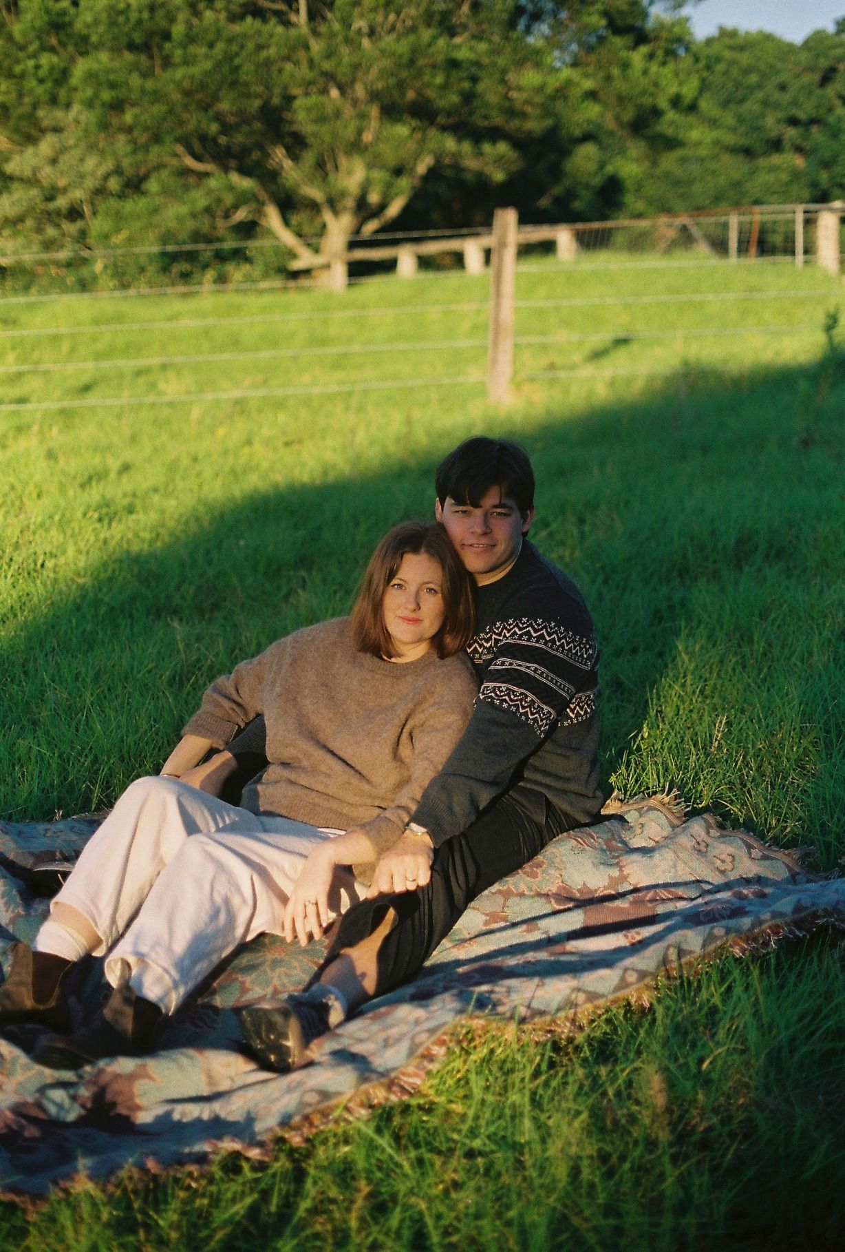 Couple relaxing together on a blanket in a green pastoral field during a golden hour shoot.