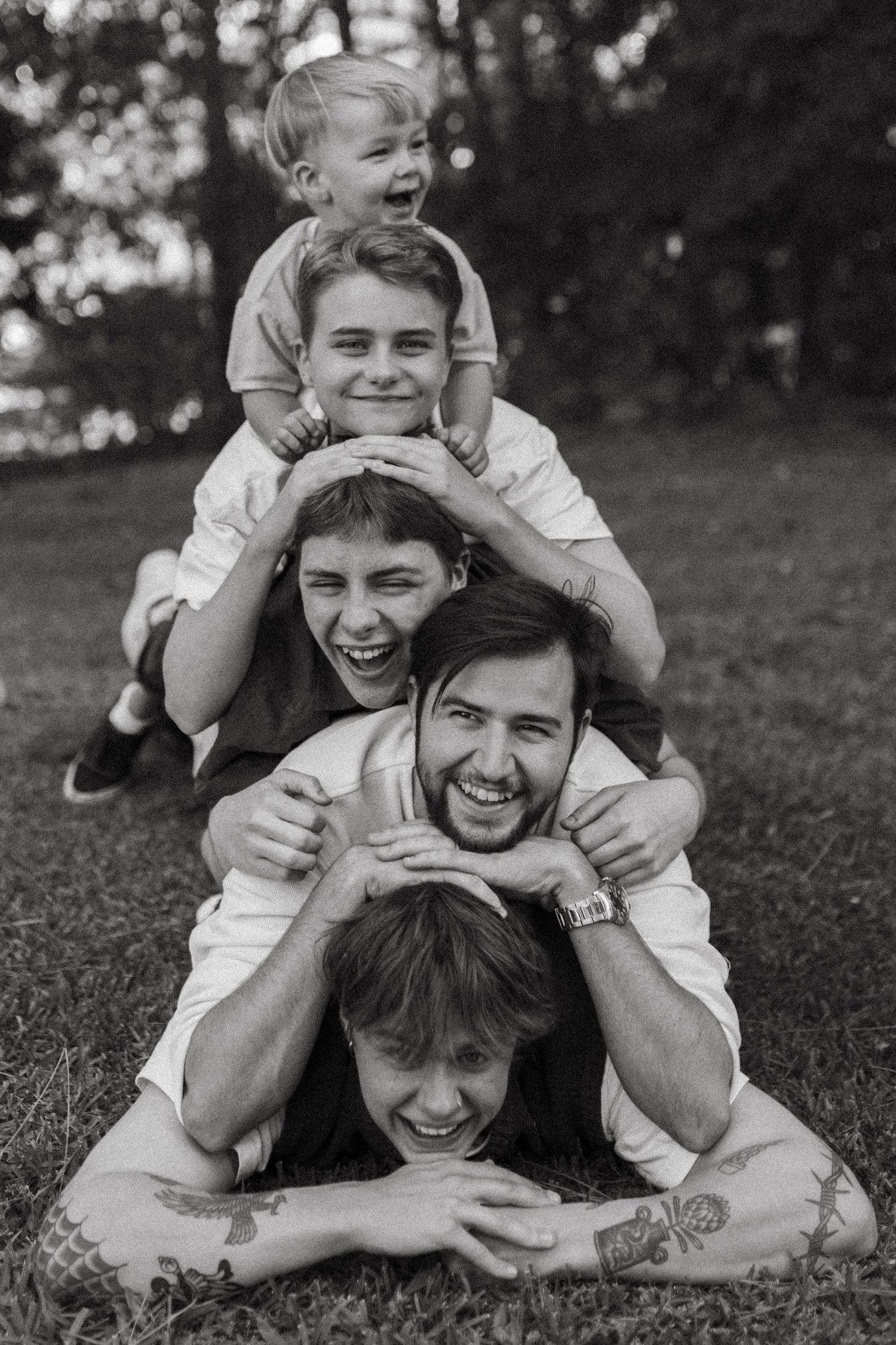 Black and white photo of four males stacked in a playful human pyramid on grass, all laughing joyfully.