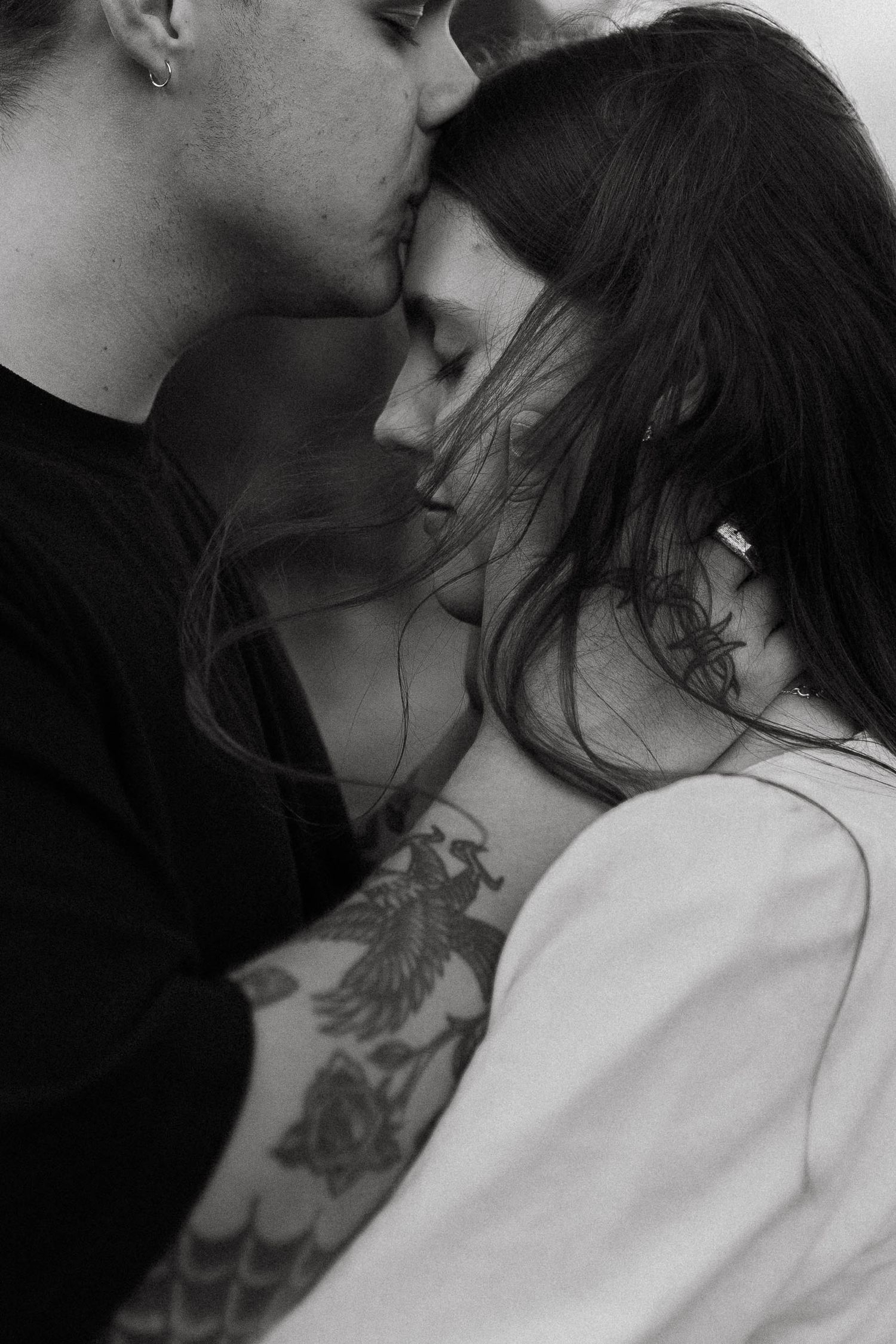 Black and white close-up of couple sharing a tender kiss, mans tattoos visible on his arm.