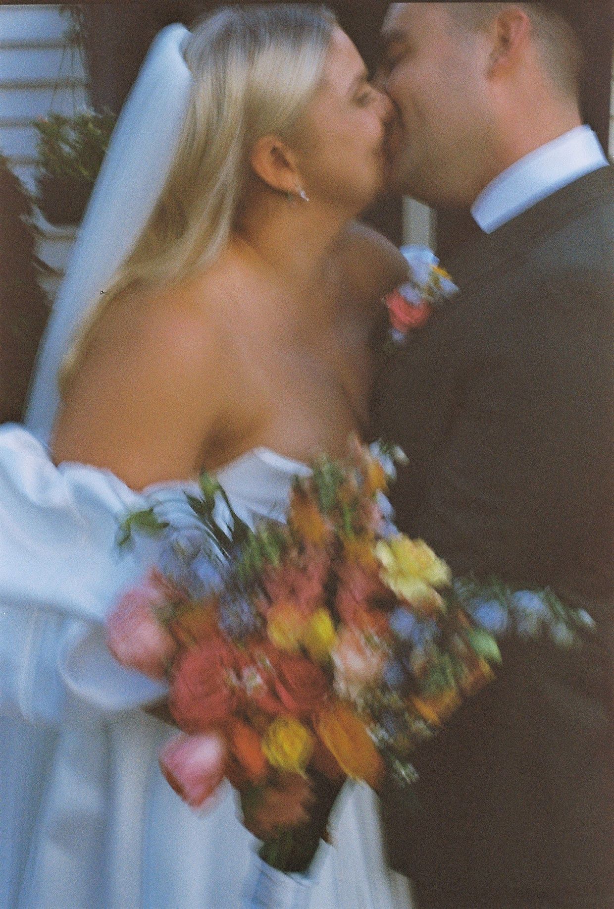 Bride and groom sharing a kiss, bride holding a vibrant colorful bouquet in a film-style photo.