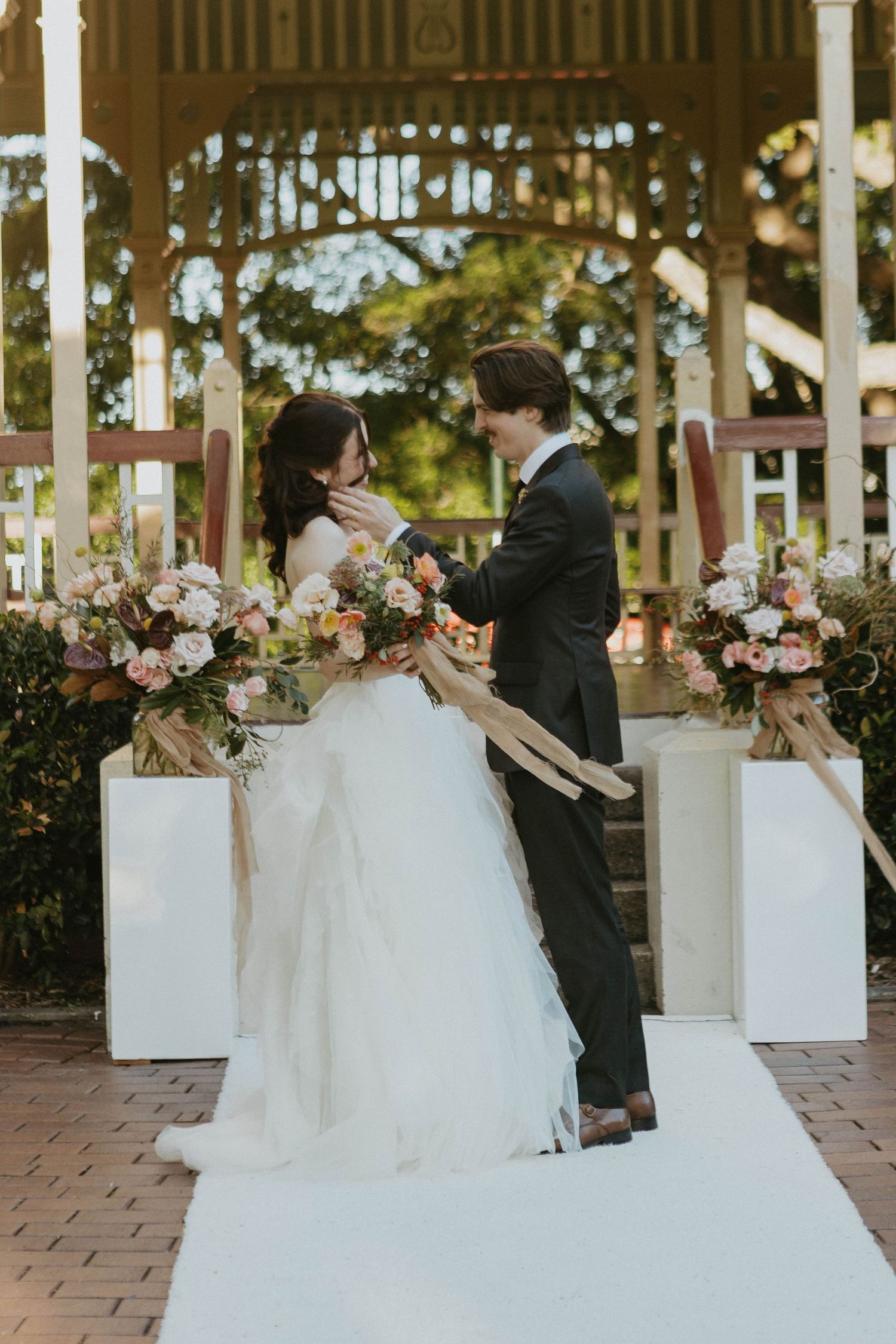 Bride and groom share a tender moment at a floral-decorated outdoor gazebo wedding ceremony.