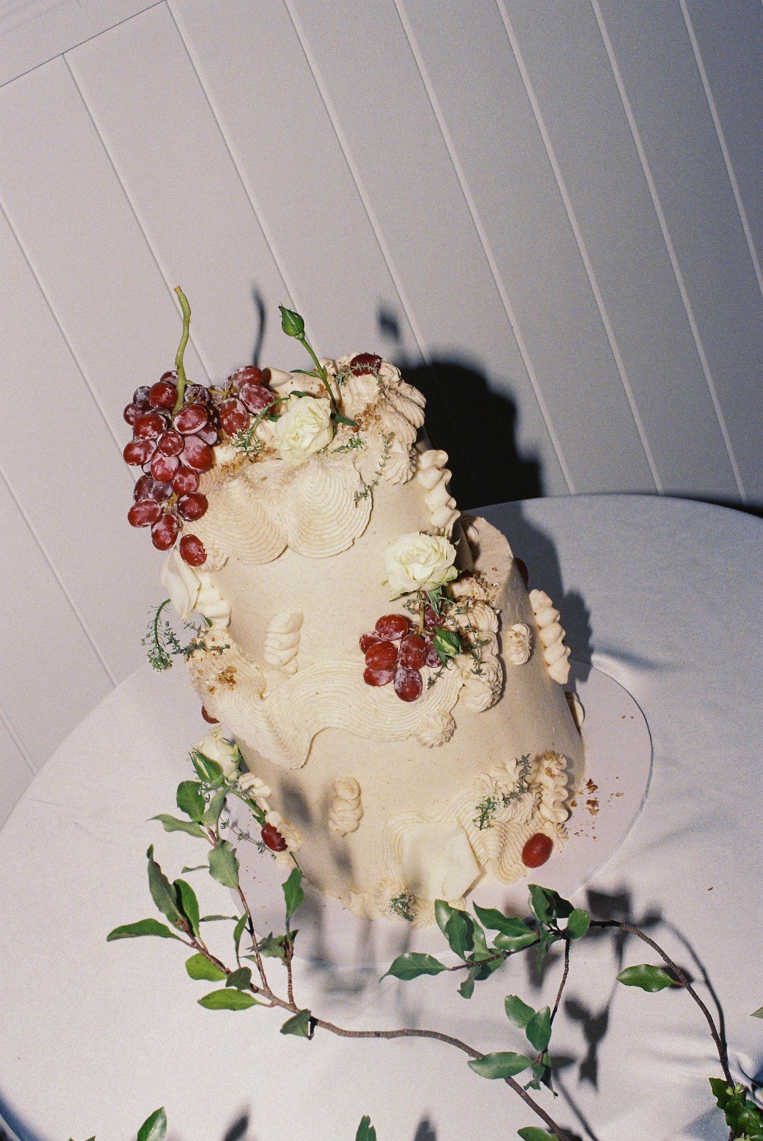 Elegant two-tier white wedding cake adorned with red berries, white flowers, and green vines on a white table.