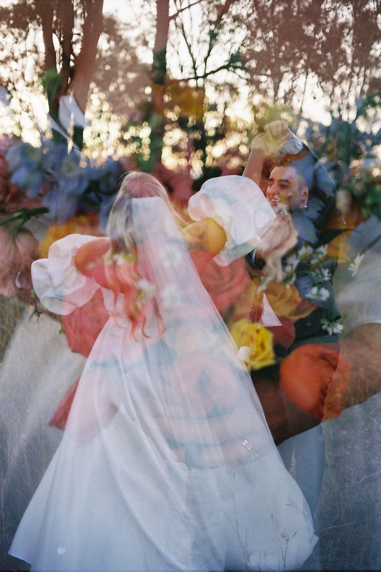 Artistic double exposure film photo of bride and groom with colorful floral backdrop.