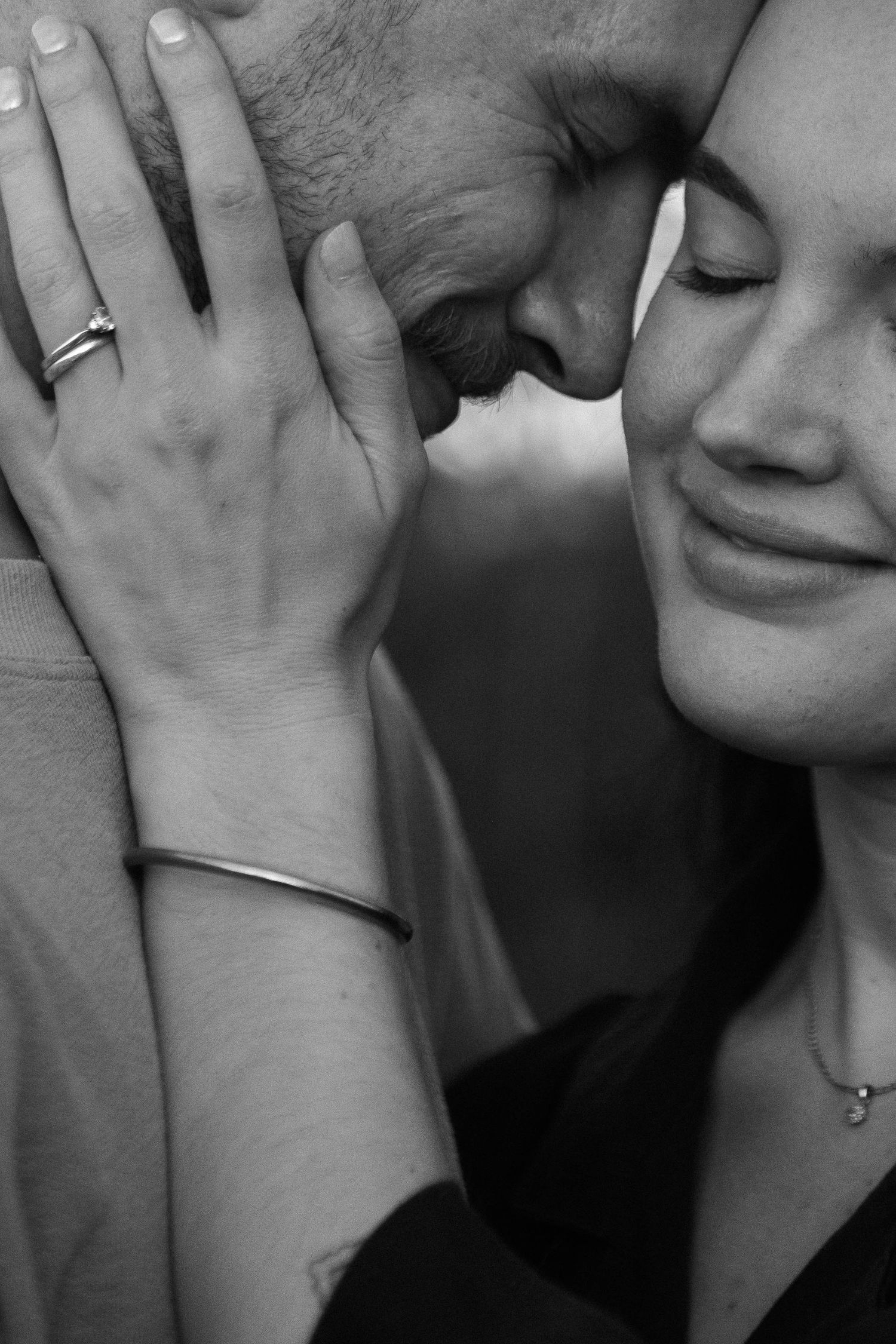 Black and white photo of a couple sharing an intimate moment, woman smiling with eyes closed, wearing an engagement ring.