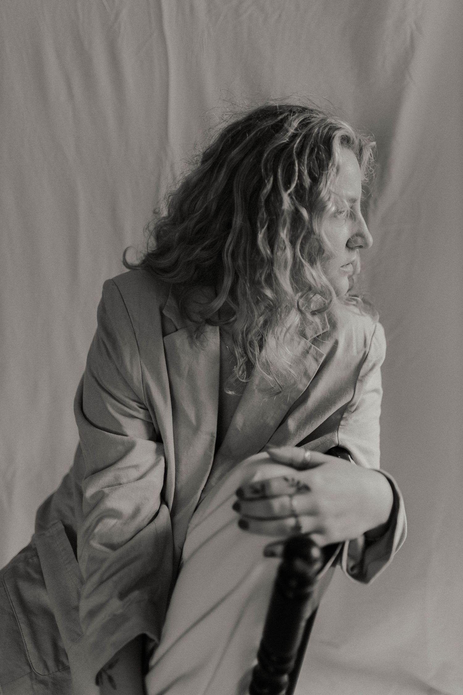 Black and white side profile of curly-haired woman in blazer seated on chair, looking away.