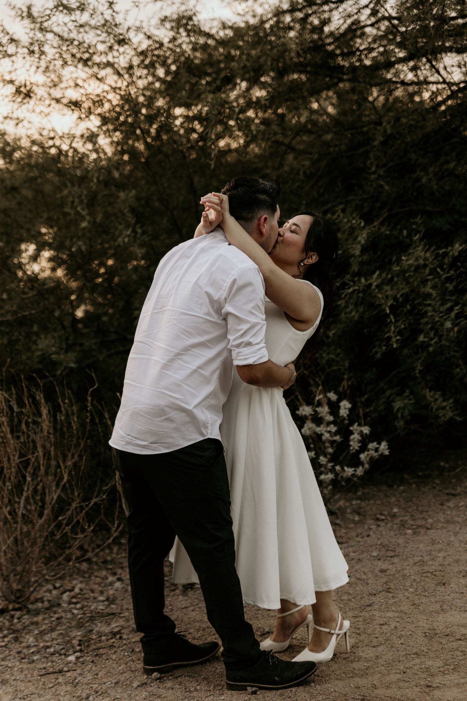 A couple embracing in a romantic outdoor setting with trees and nature in the background.
