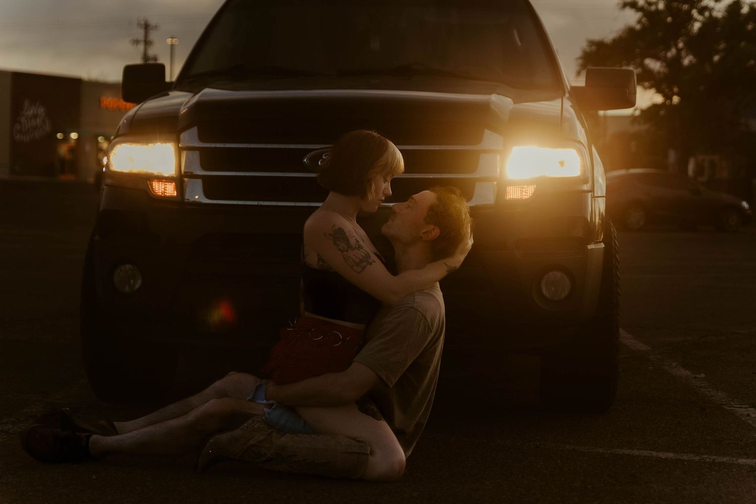 Couple sharing a romantic embrace in front of a truck at golden hour sunset in a parking lot.