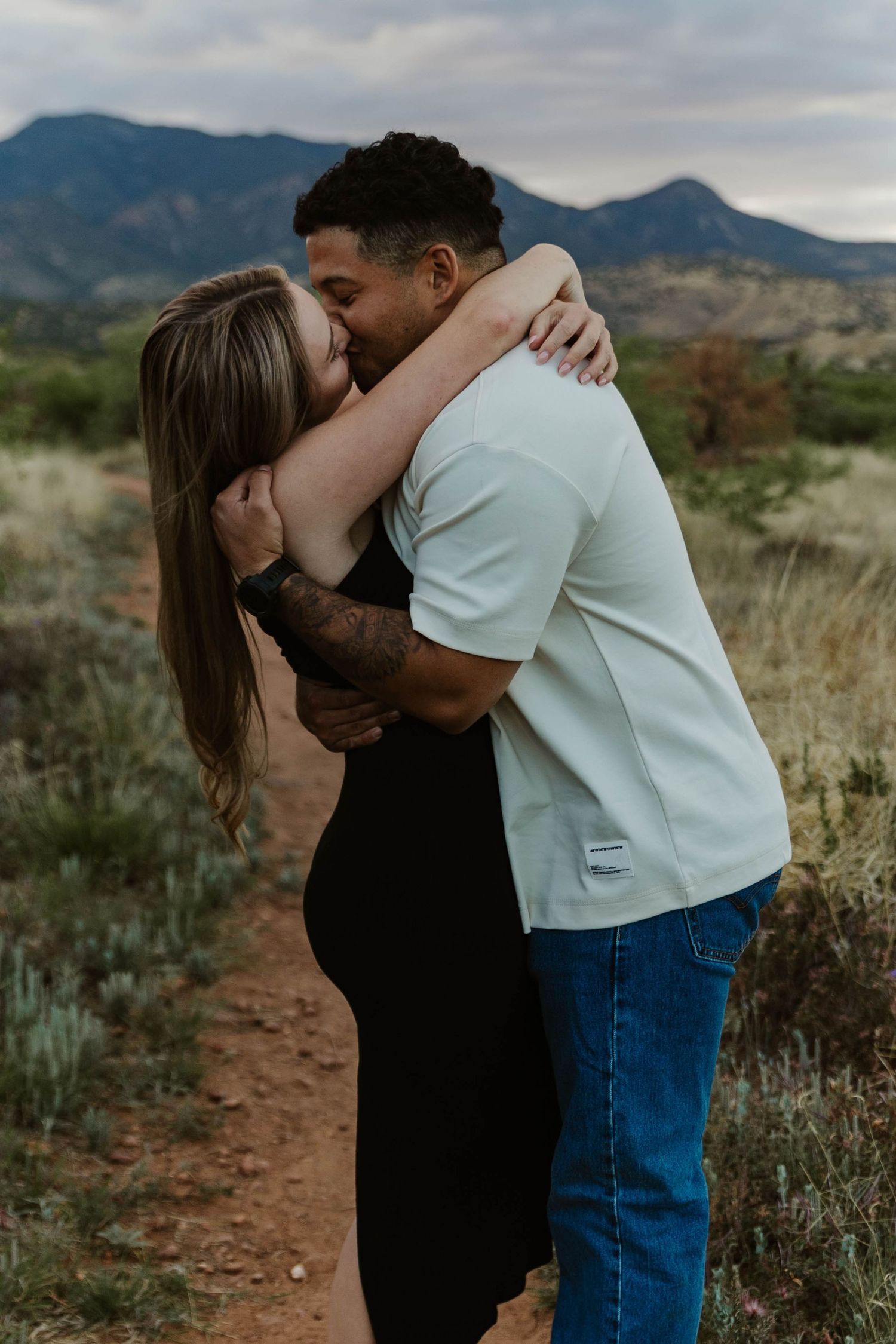 Couple sharing a romantic kiss outdoors in a desert landscape with mountains in the background.