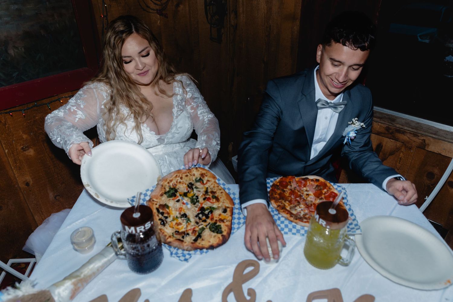 Wedding reception table with various pizzas and drinks being shared by guests.