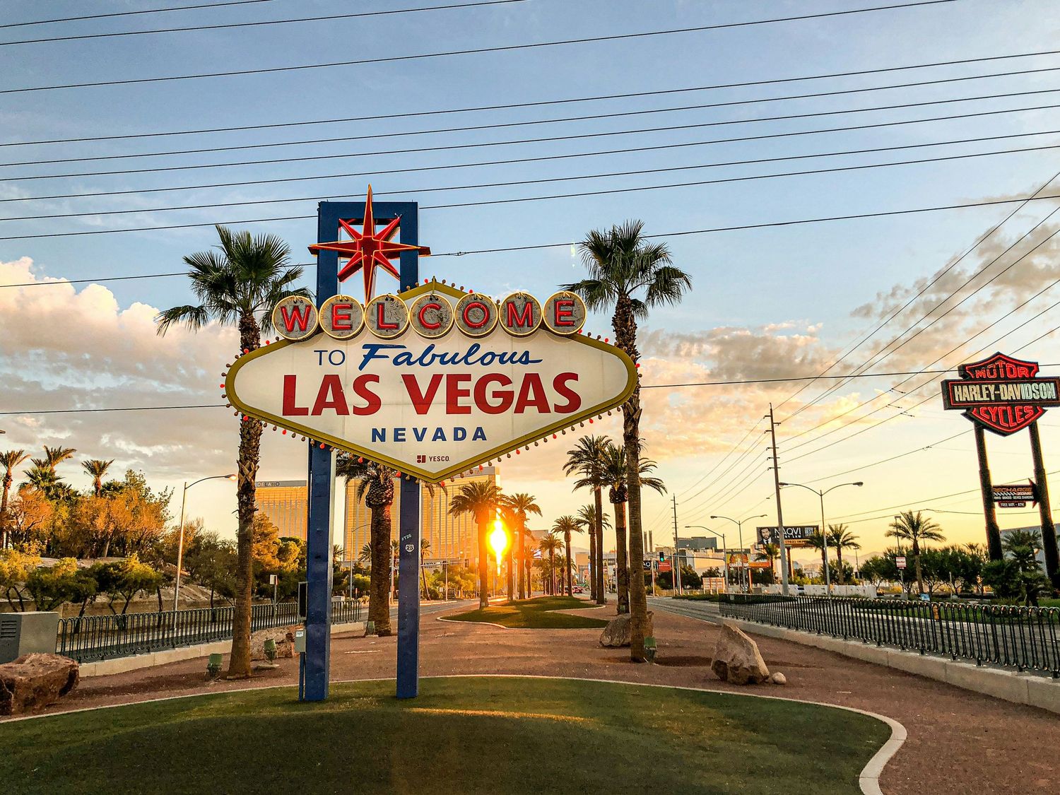 The iconic Welcome to Fabulous Las Vegas Nevada sign glows at sunset with palm trees and blue skies in the background.