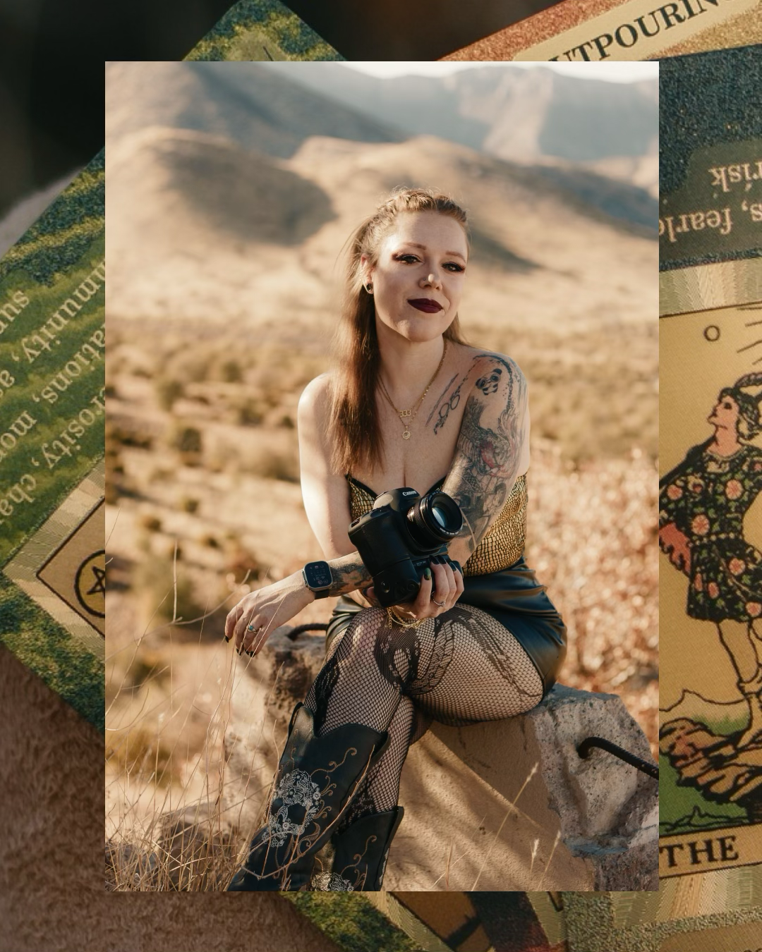 Tattooed woman in bohemian outfit sitting outdoors in desert landscape surrounded by tarot cards.