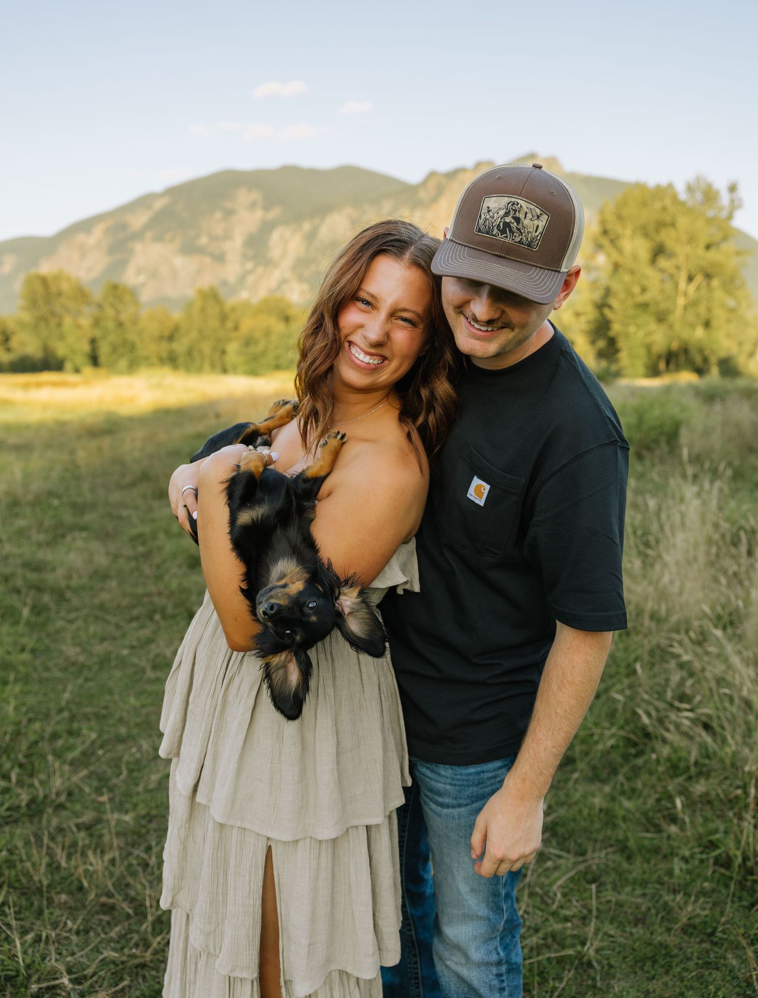 Couple posing with their dog in a sunlit field during an outdoor couples photography session in Washington.