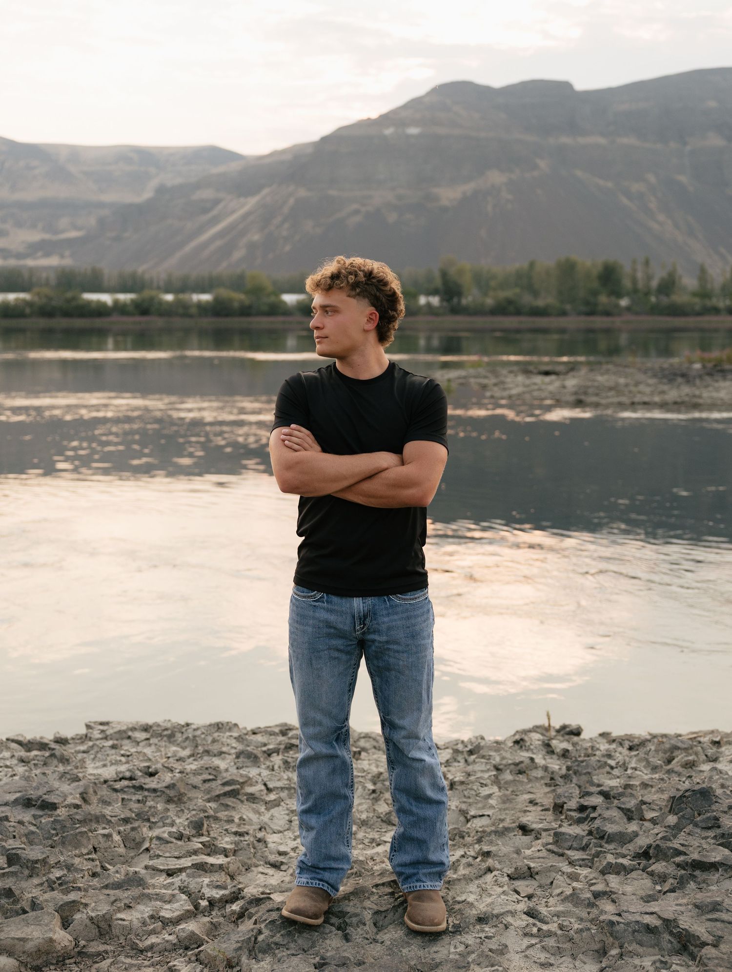 High school senior standing along the river with scenic mountain views during a golden hour senior photography session.