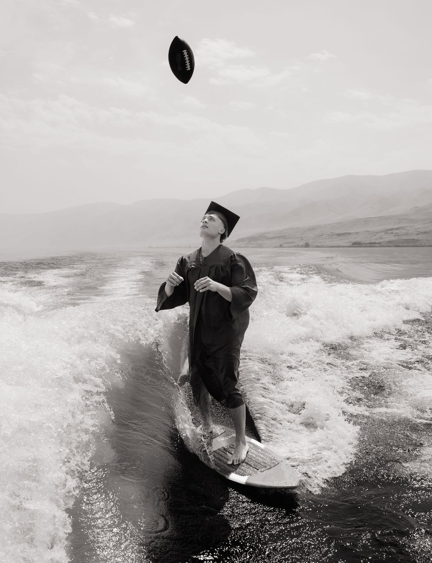 High school graduate wakesurfing in his cap and gown during a creative Washington senior photography session.