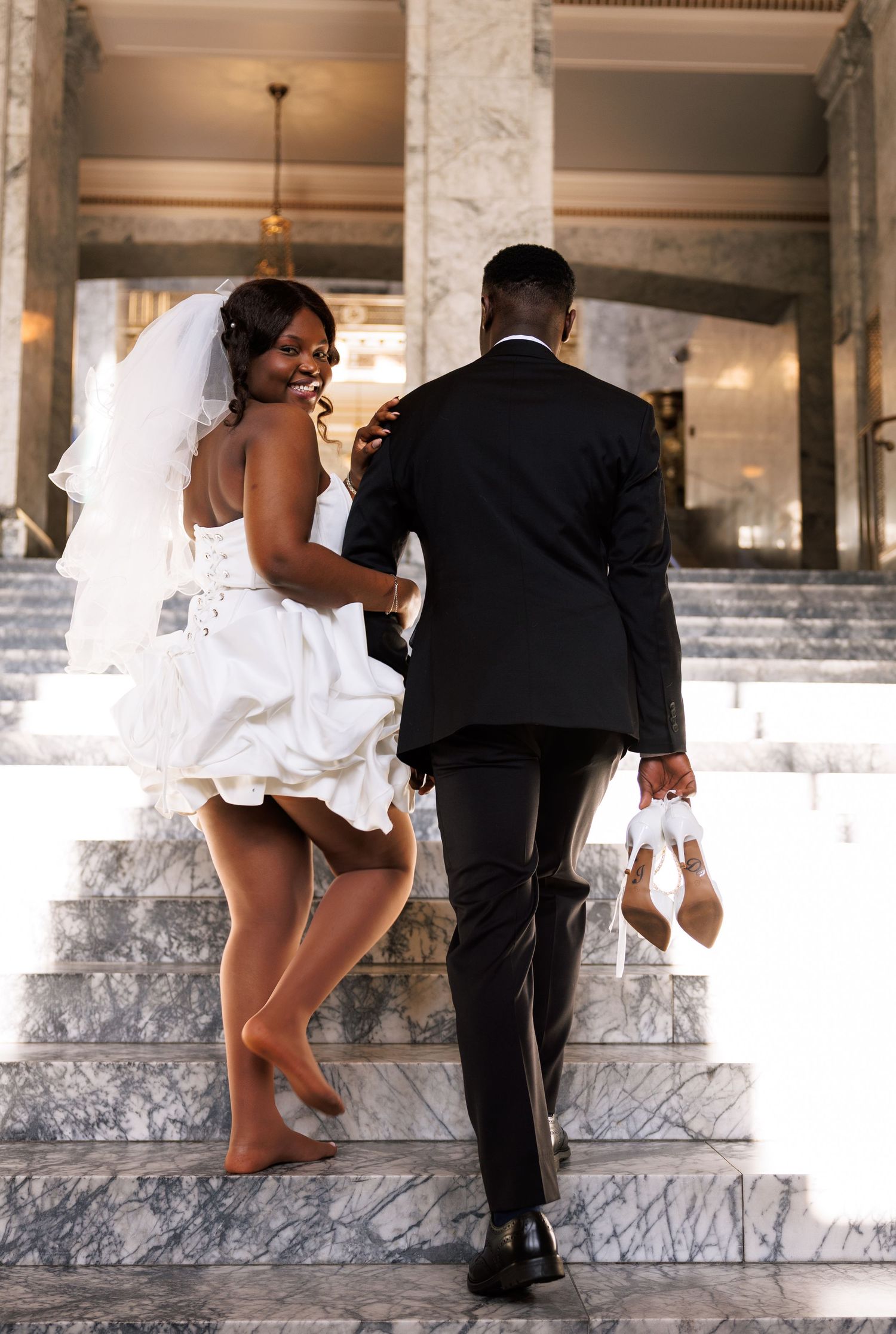 Bride smiling back while walking up the Capitol stairs with her groom in Olympia