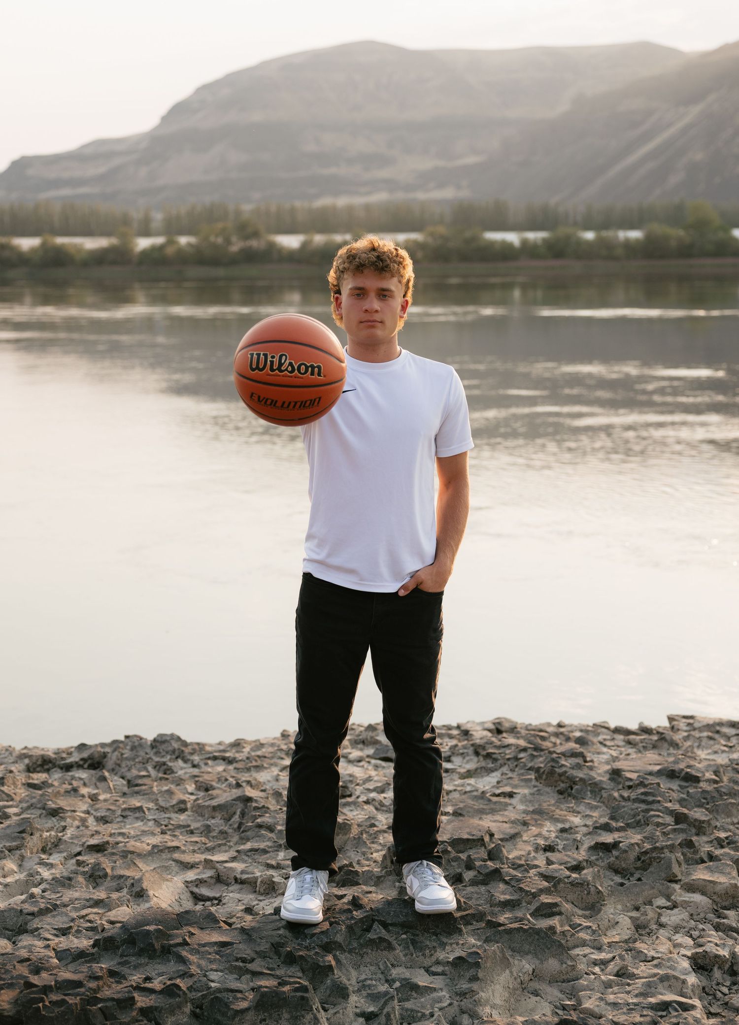 High school senior posing with a basketball by the water with mountain views during a Washington senior portrait session.
