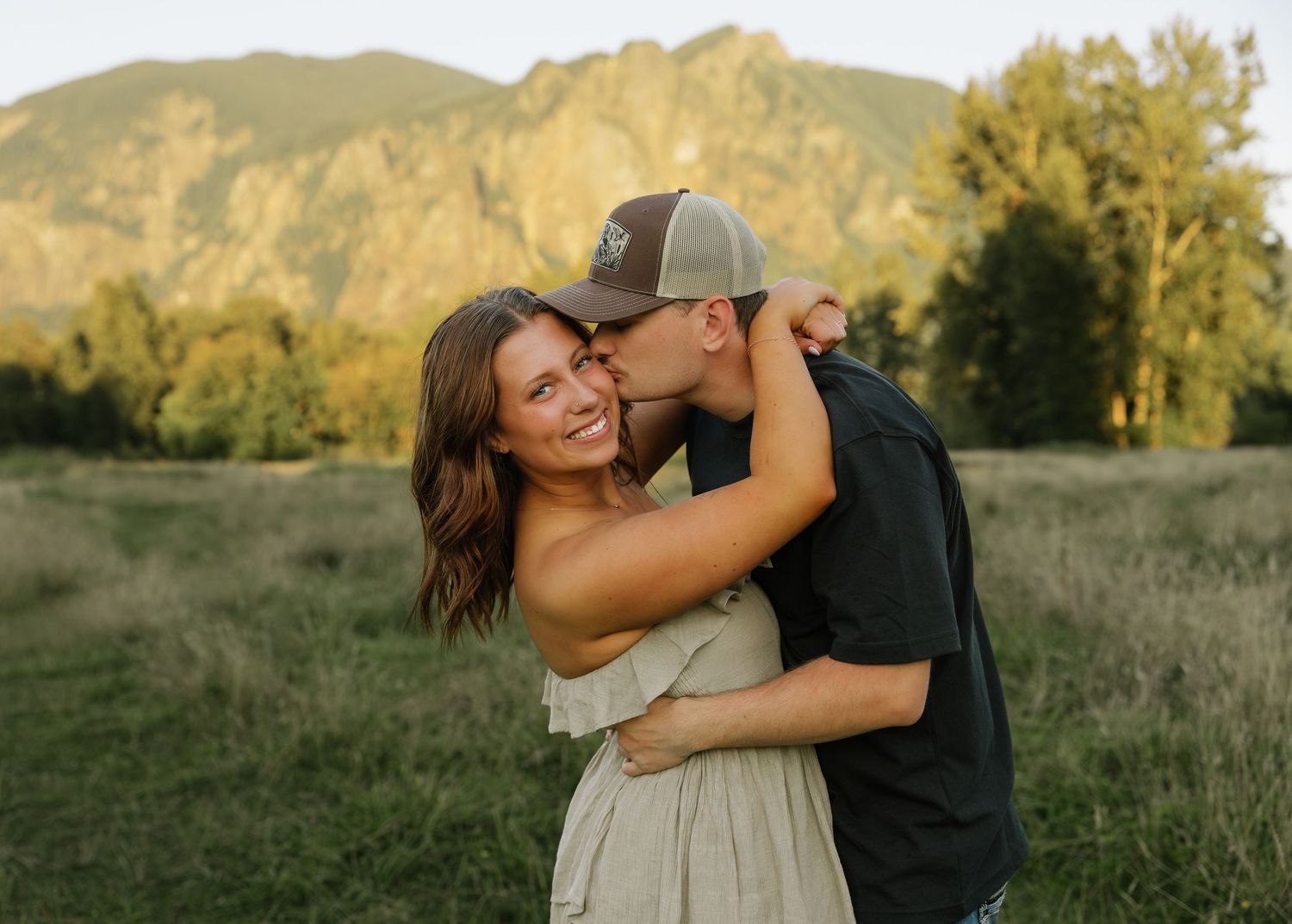 Couple embracing in a grassy field with mountain views during a romantic Washington couples photography session.