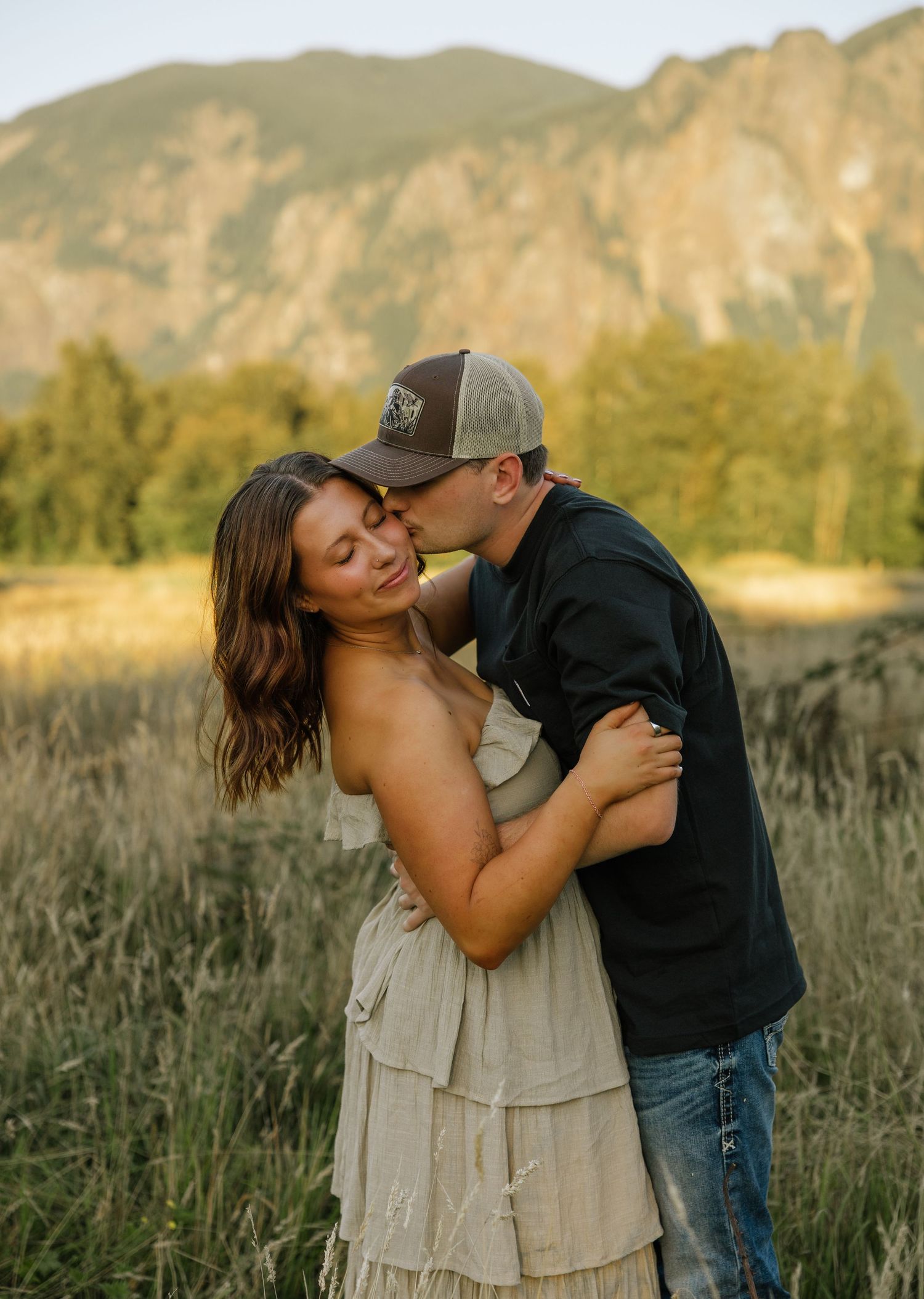 Couple laughing and embracing in a field with mountain views during a Washington couples photography session.