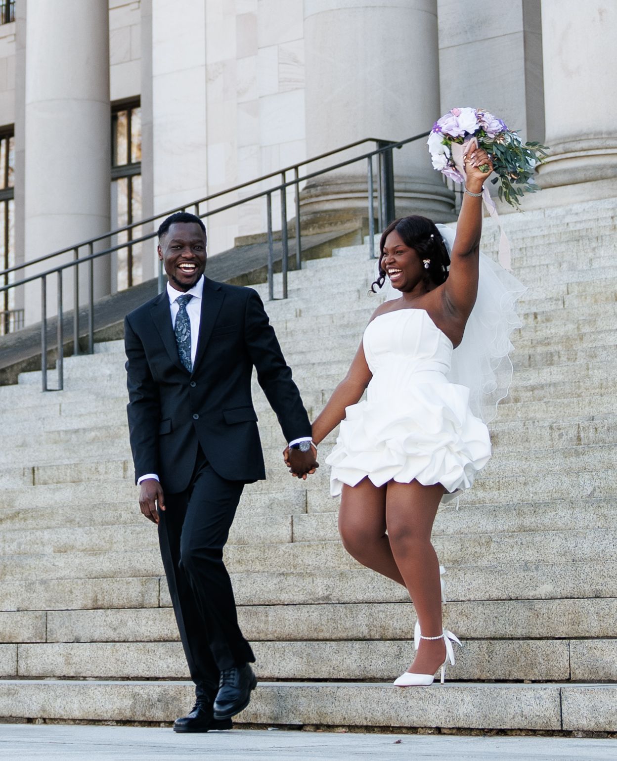 Bride celebrating with her bouquet while walking down the Washington State Capitol steps with her groom