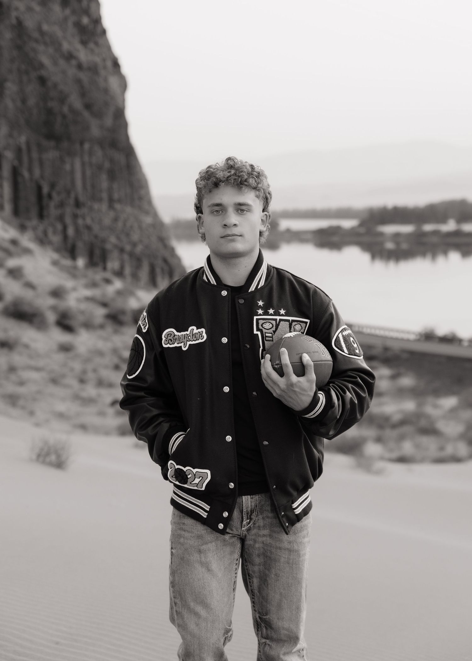 Black and white senior portrait with a football and letterman jacket overlooking the mountains in Washington.