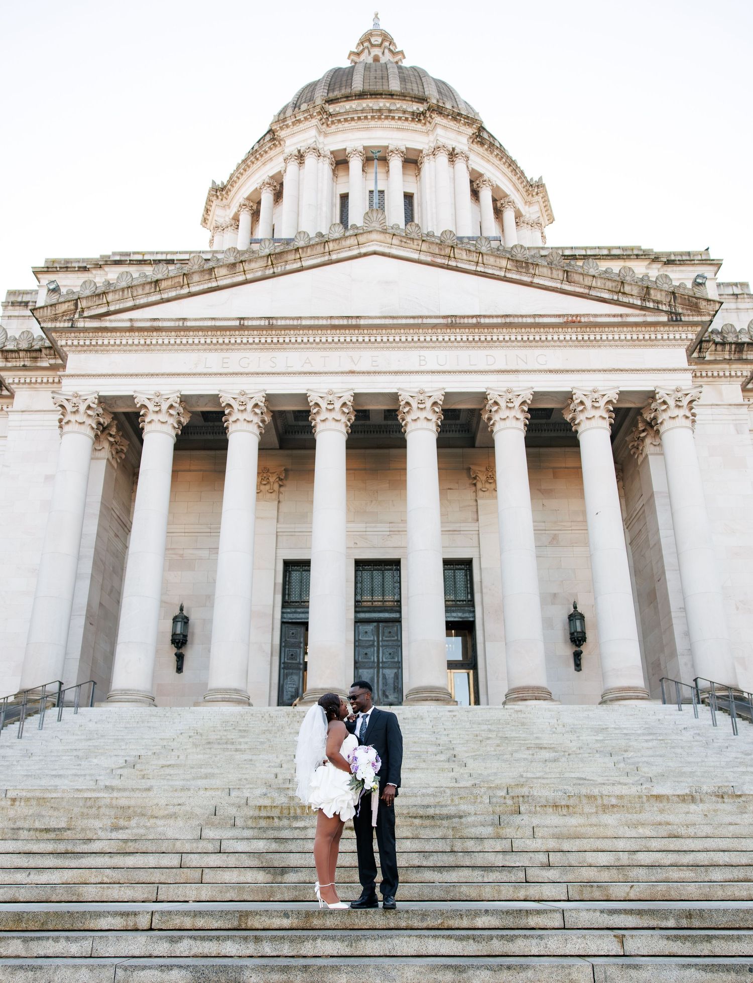 Bride and groom standing beneath the grand columns of the Washington State Capitol in Olympia
