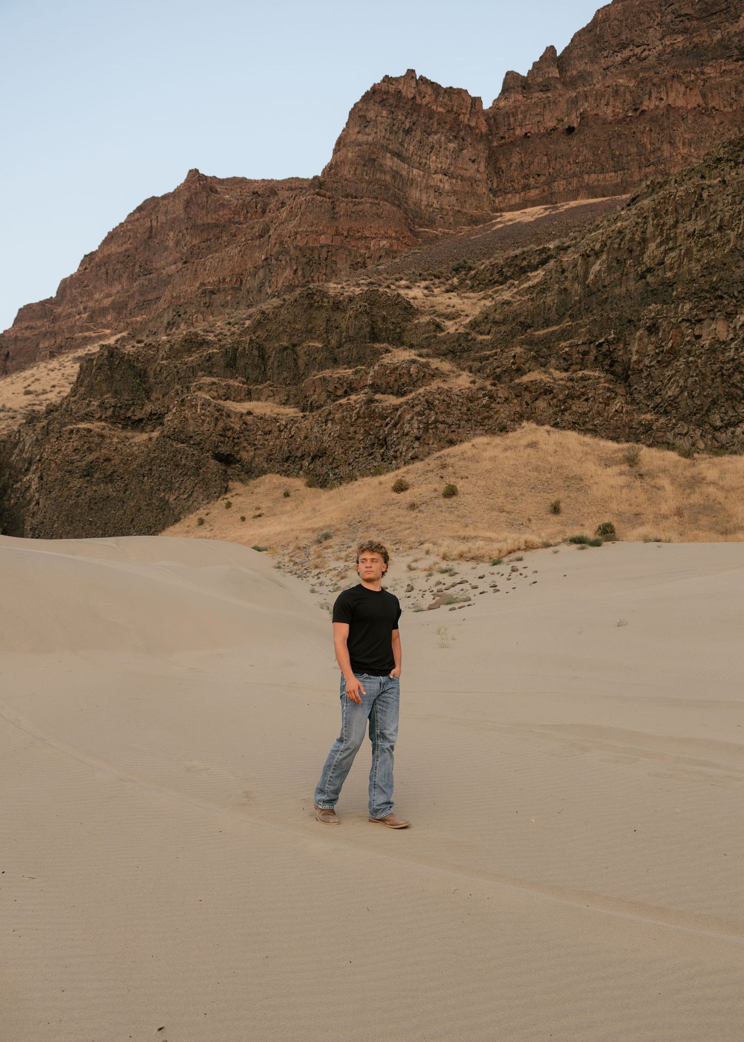 High school senior standing in a dramatic desert landscape surrounded by rugged cliffs during an outdoor senior session.