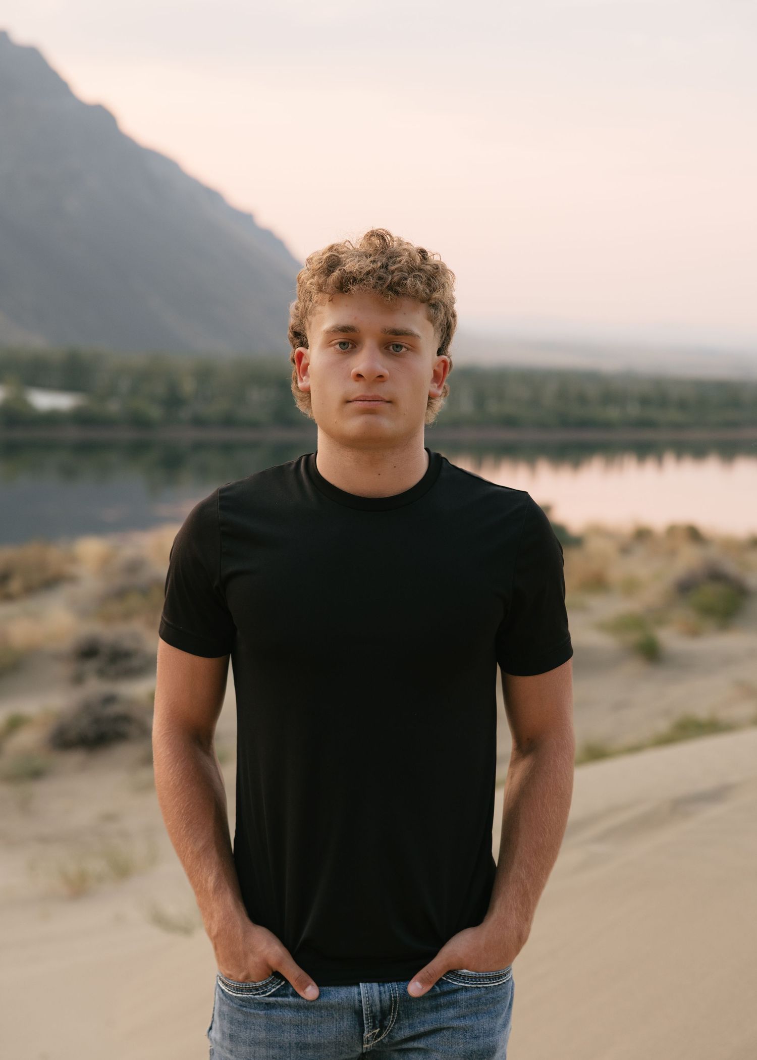High school senior portrait by the water at sunset with scenic mountains in the background.