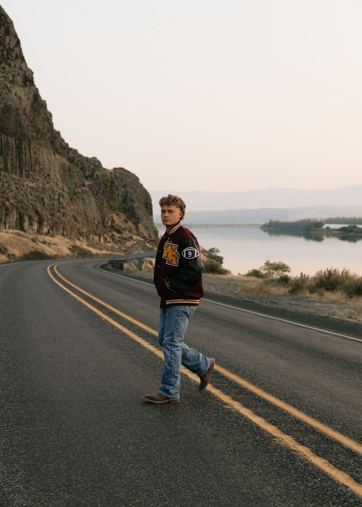 High school senior walking along a scenic road surrounded by mountains during a Washington senior portrait session.