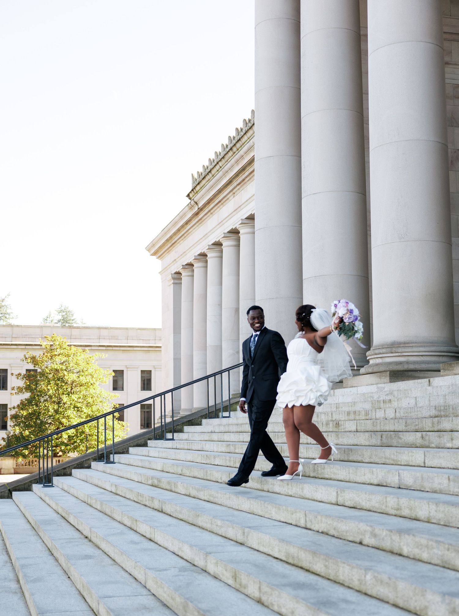 Bride celebrating with her bouquet while walking with her groom on the Washington State Capitol steps