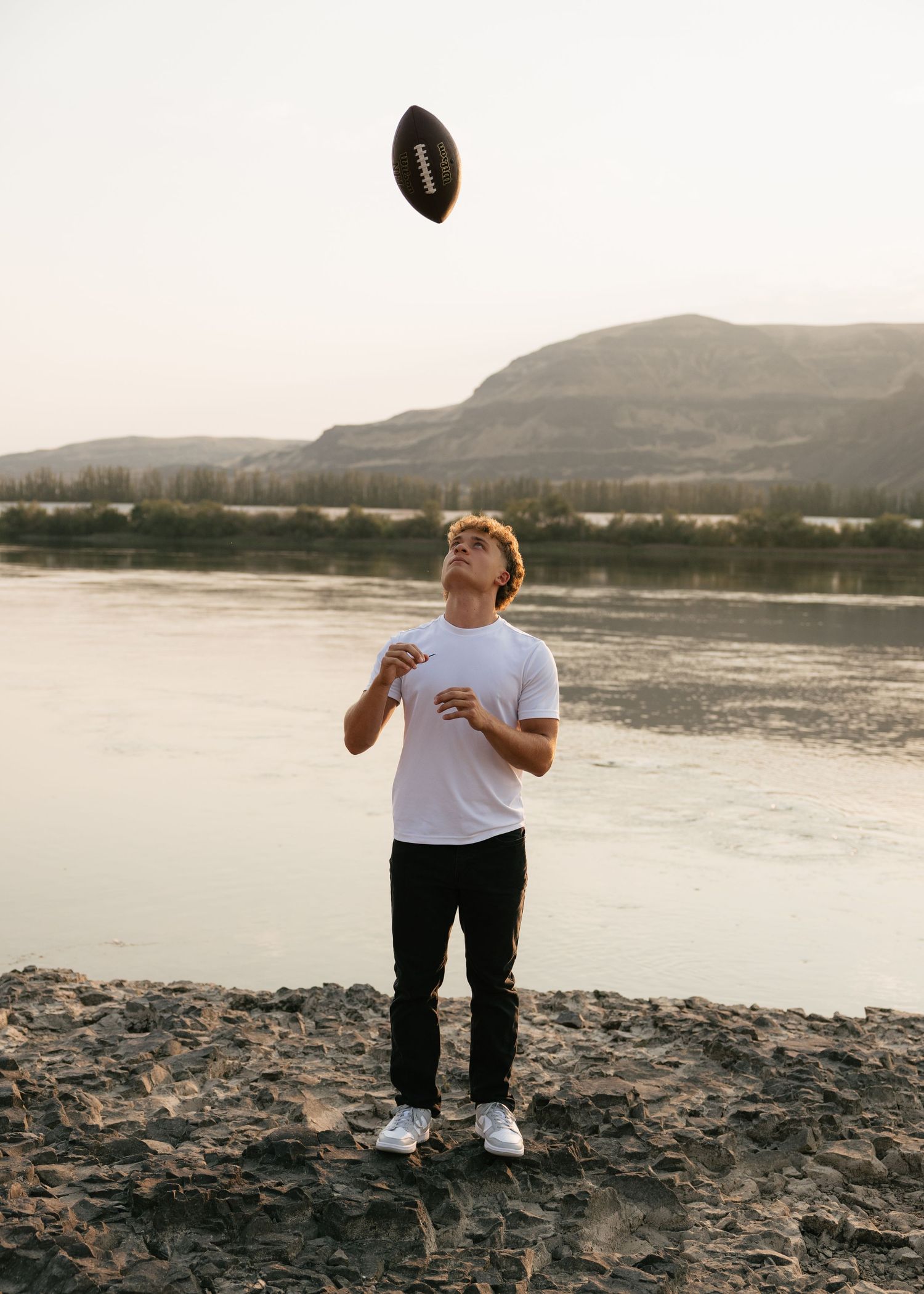 High school senior tossing a football by the water during a fun outdoor Washington senior portrait session.