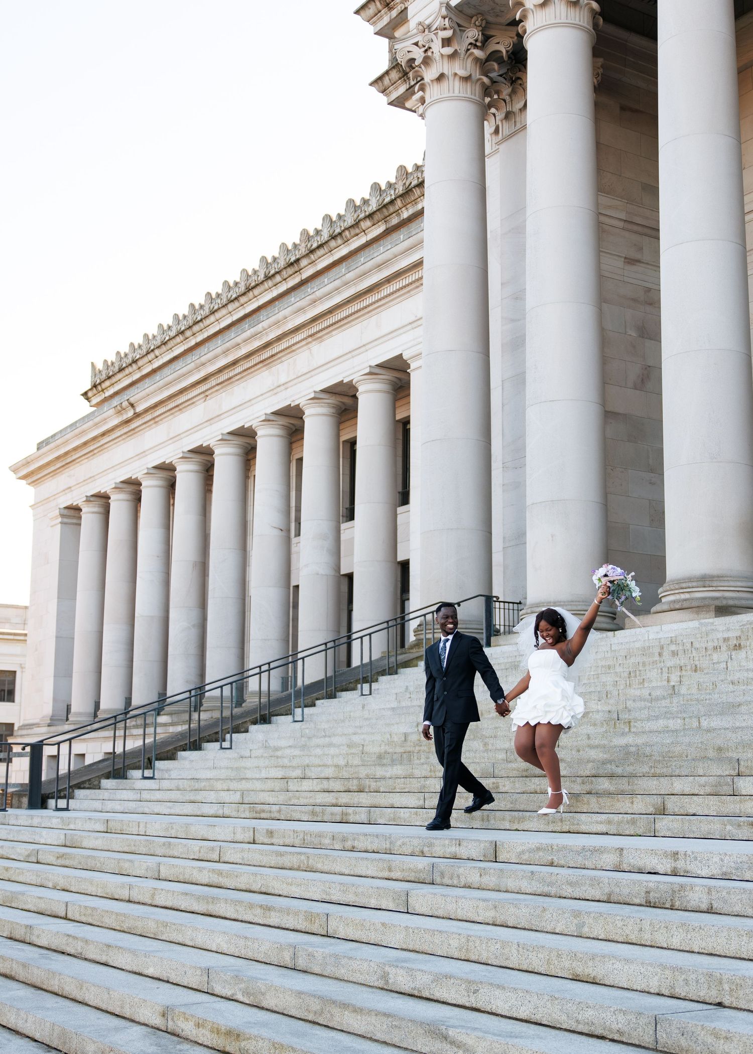 Bride celebrating with her bouquet while walking with her groom outside the Washington State Capitol