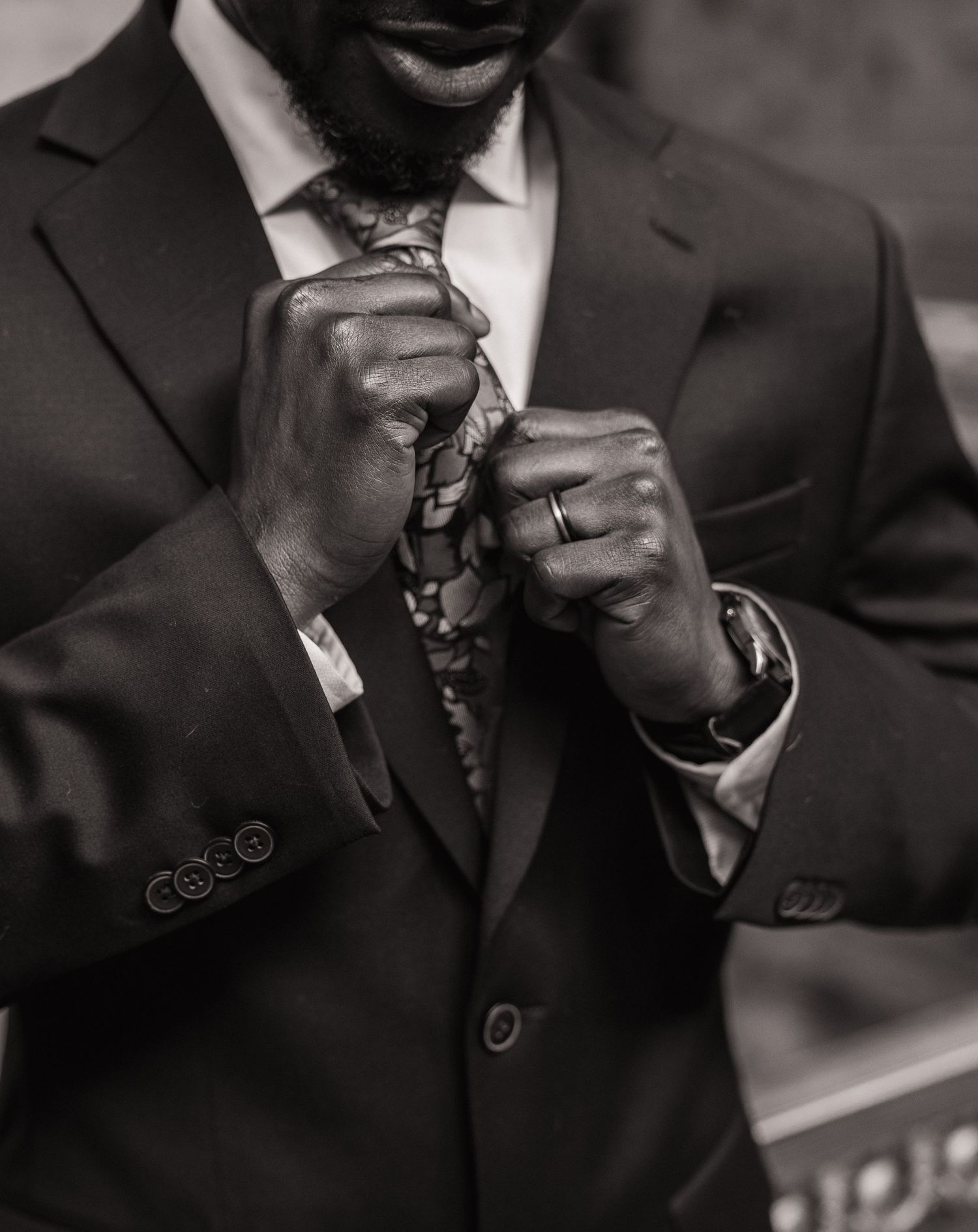 Black and white detail photo of the groom adjusting his tie on his wedding day
