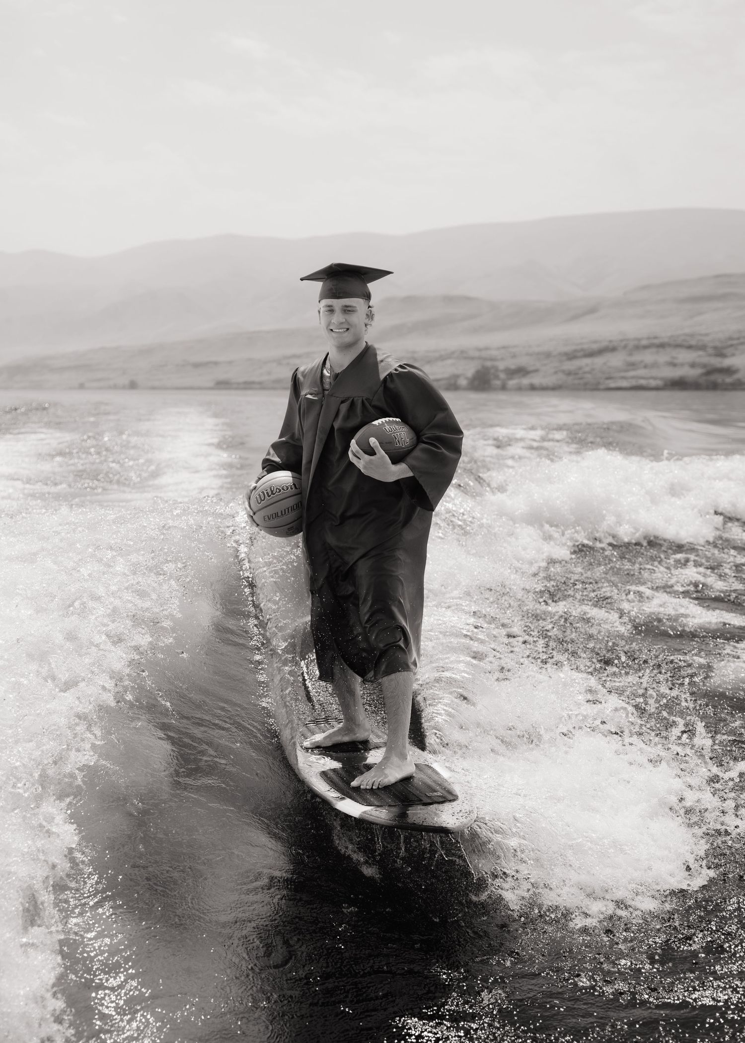 High school graduate wakesurfing in his cap and gown during a creative Washington senior photography session.