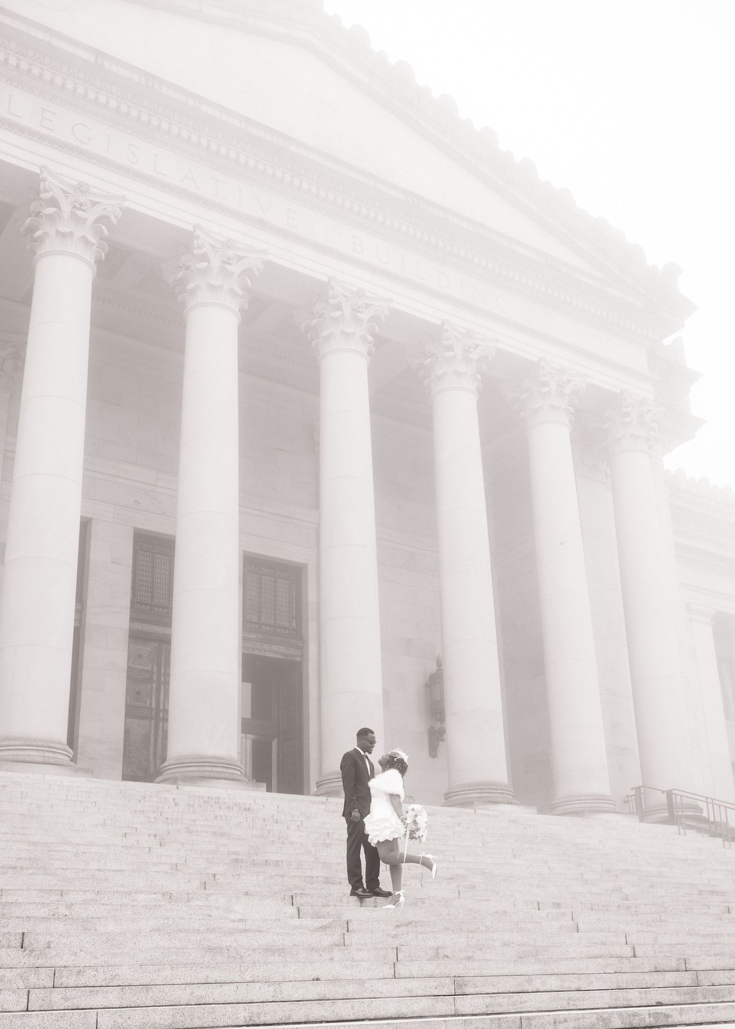 Wide wedding portrait of newlyweds beneath the columns of the Washington State Capitol in Olympia