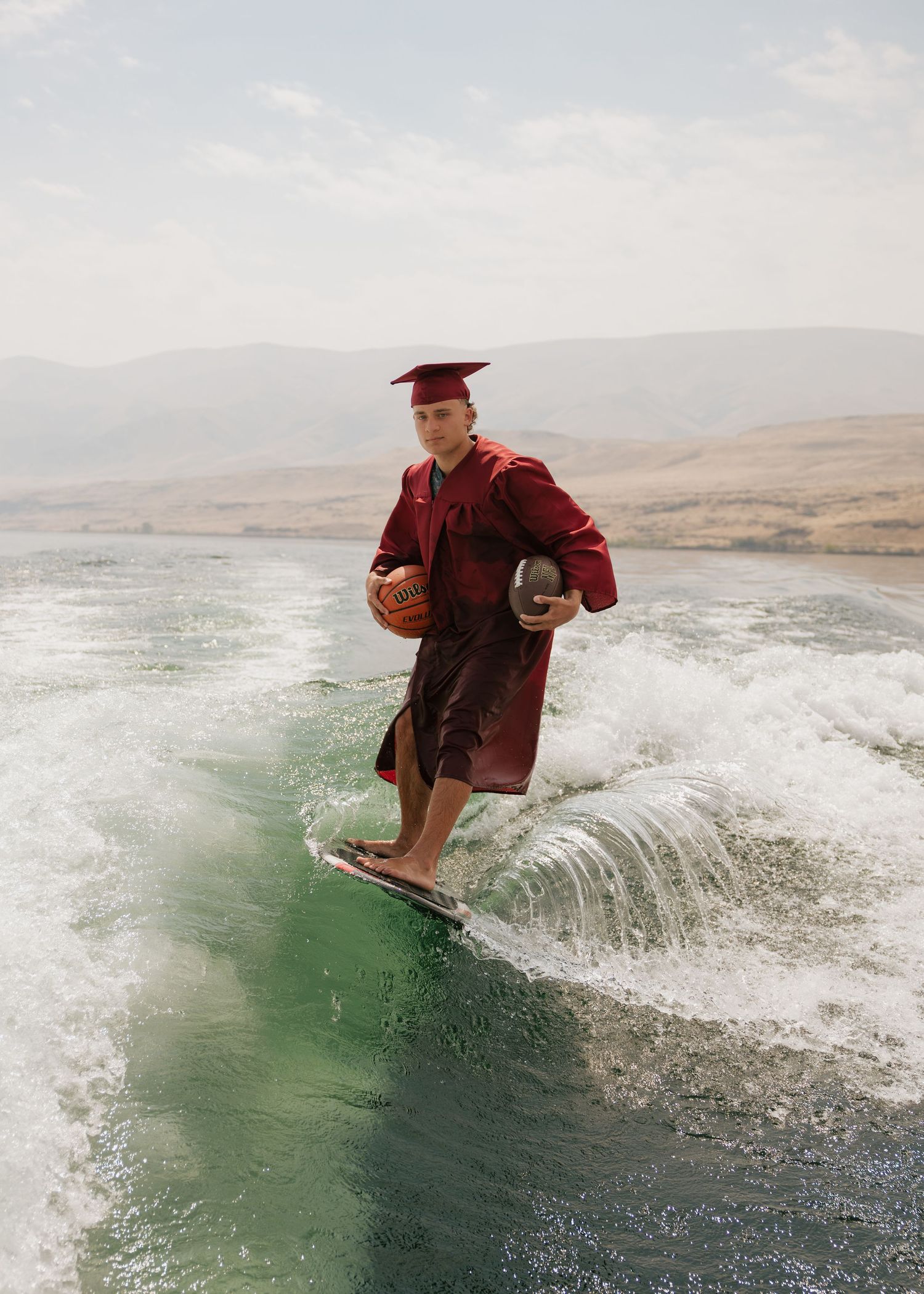 High school graduate wakesurfing in his cap and gown during a creative outdoor senior photography session.