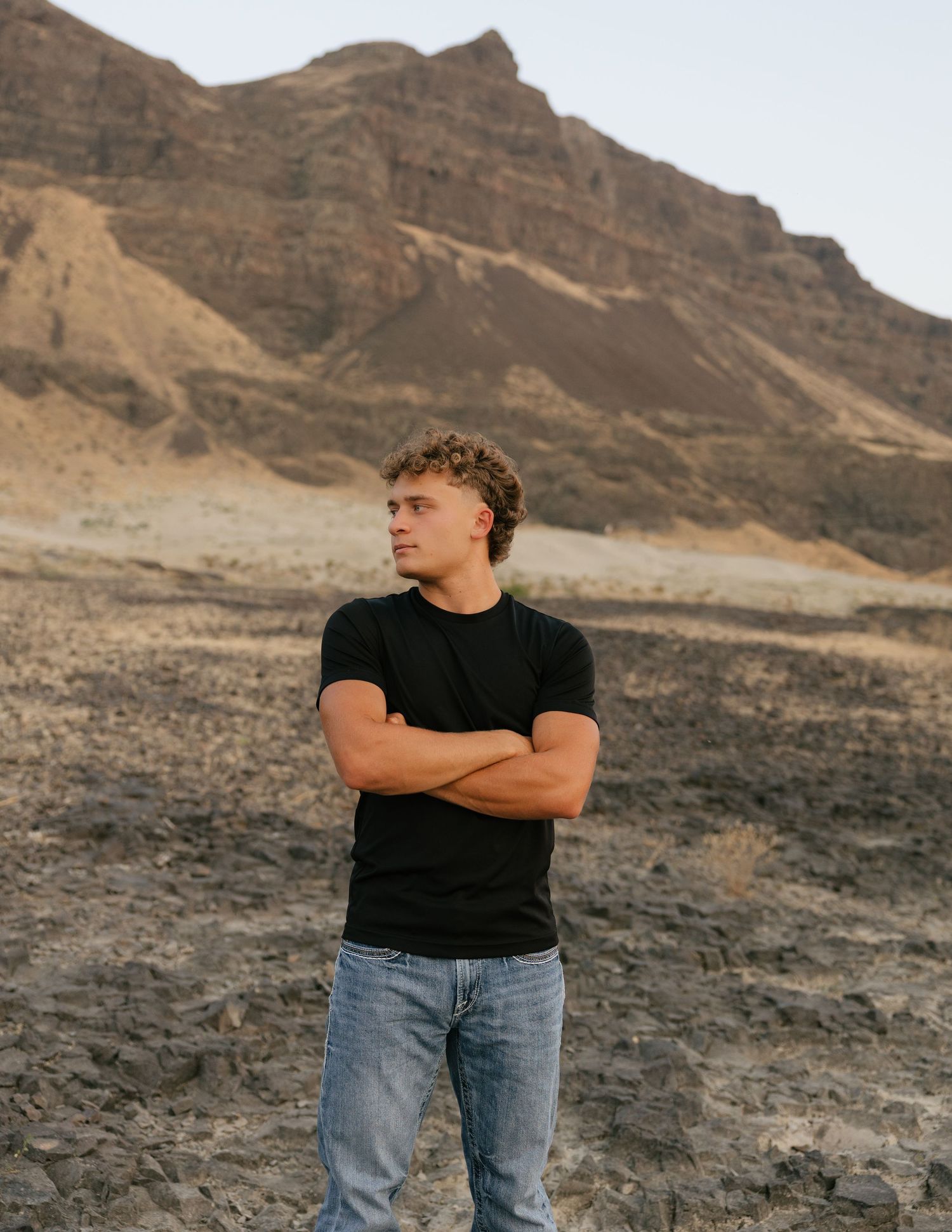 High school senior posing in a black shirt against a rugged mountain landscape during an outdoor senior session.